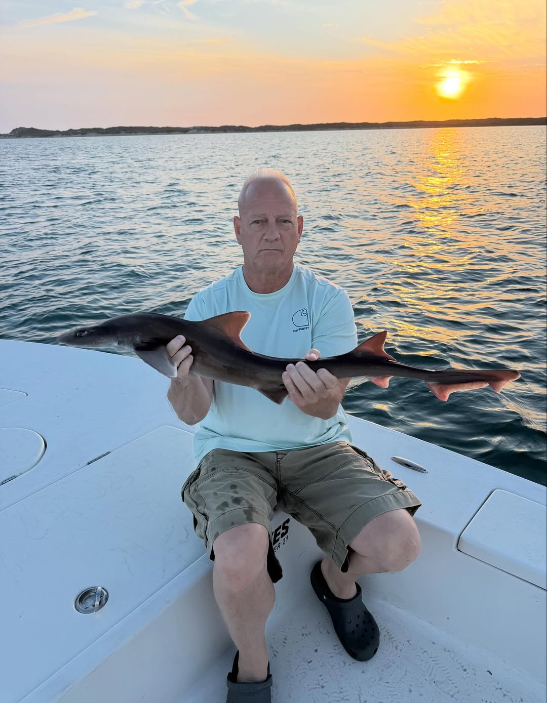 Angler holding caught fish on boat at sunset near Cedar Point NC