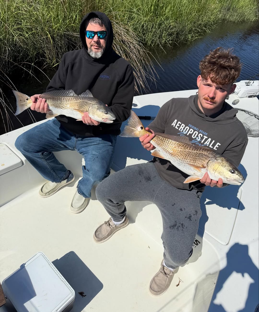 Two anglers displaying caught redfish on boat deck near marsh grass at Cedar Point NC