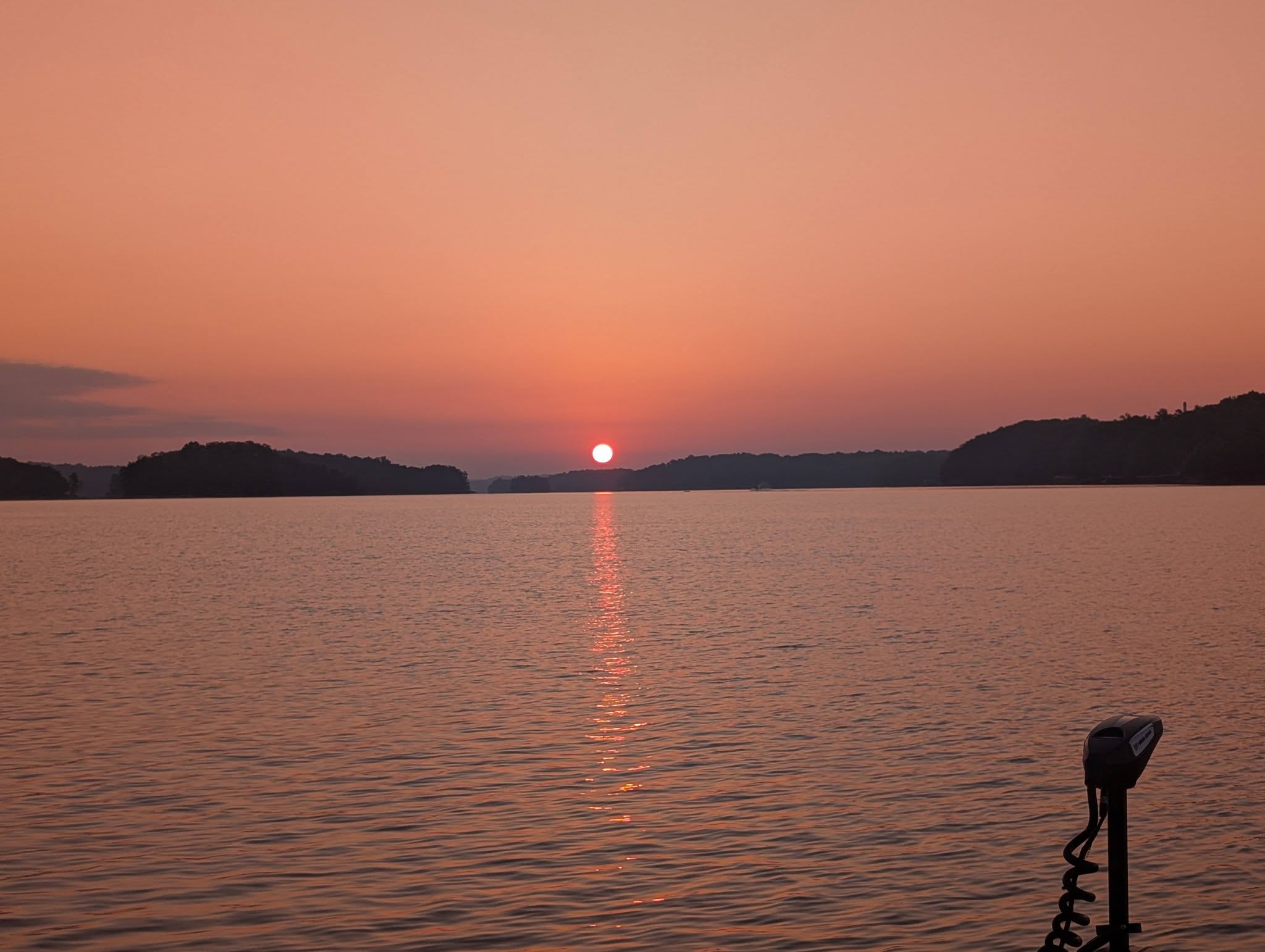 Sunset over calm lake waters with fishing boat motor visible in foreground near Gainesville GA
