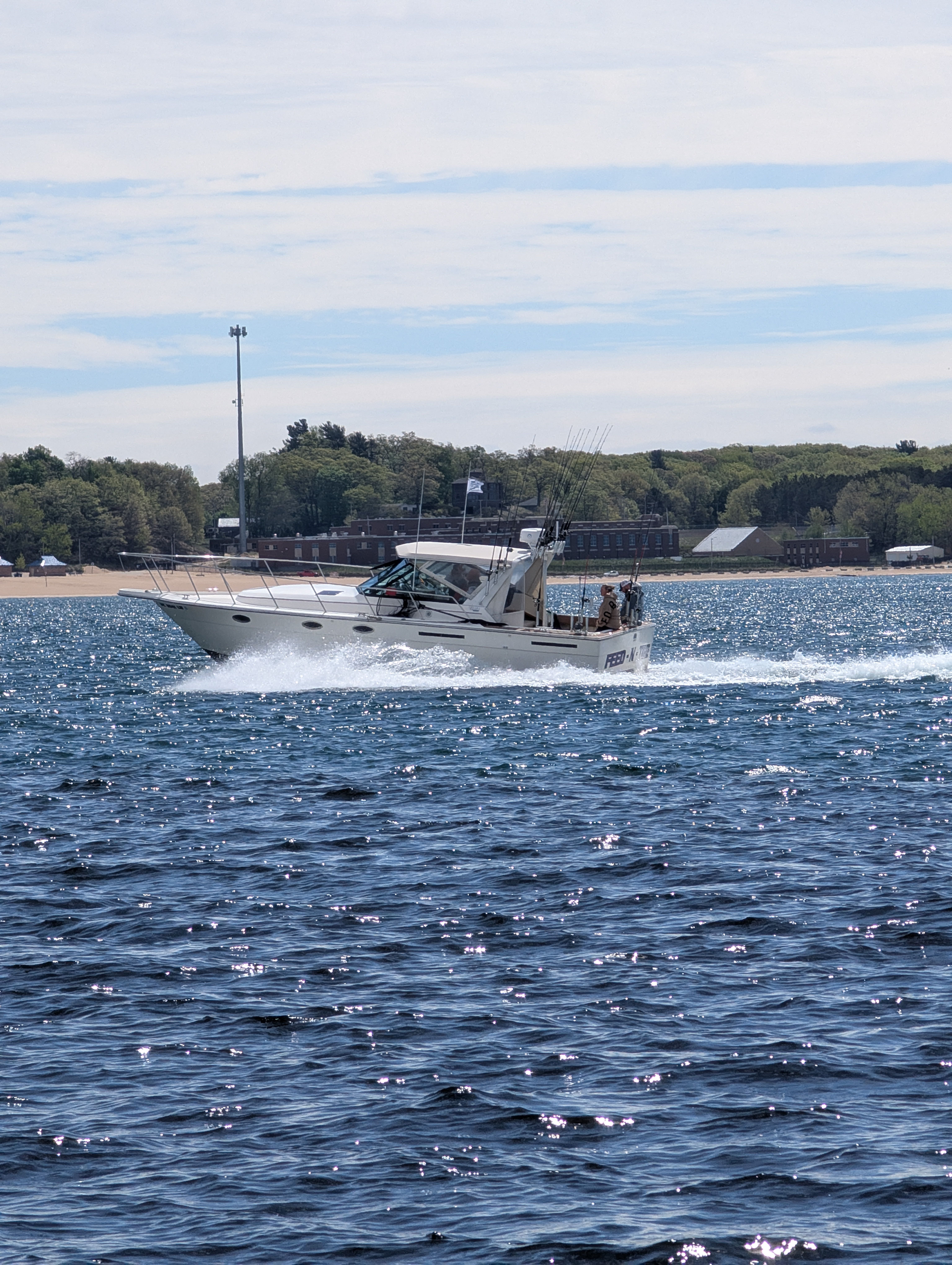 White fishing boat cruising through blue water near Muskegon MI with fishing rods visible