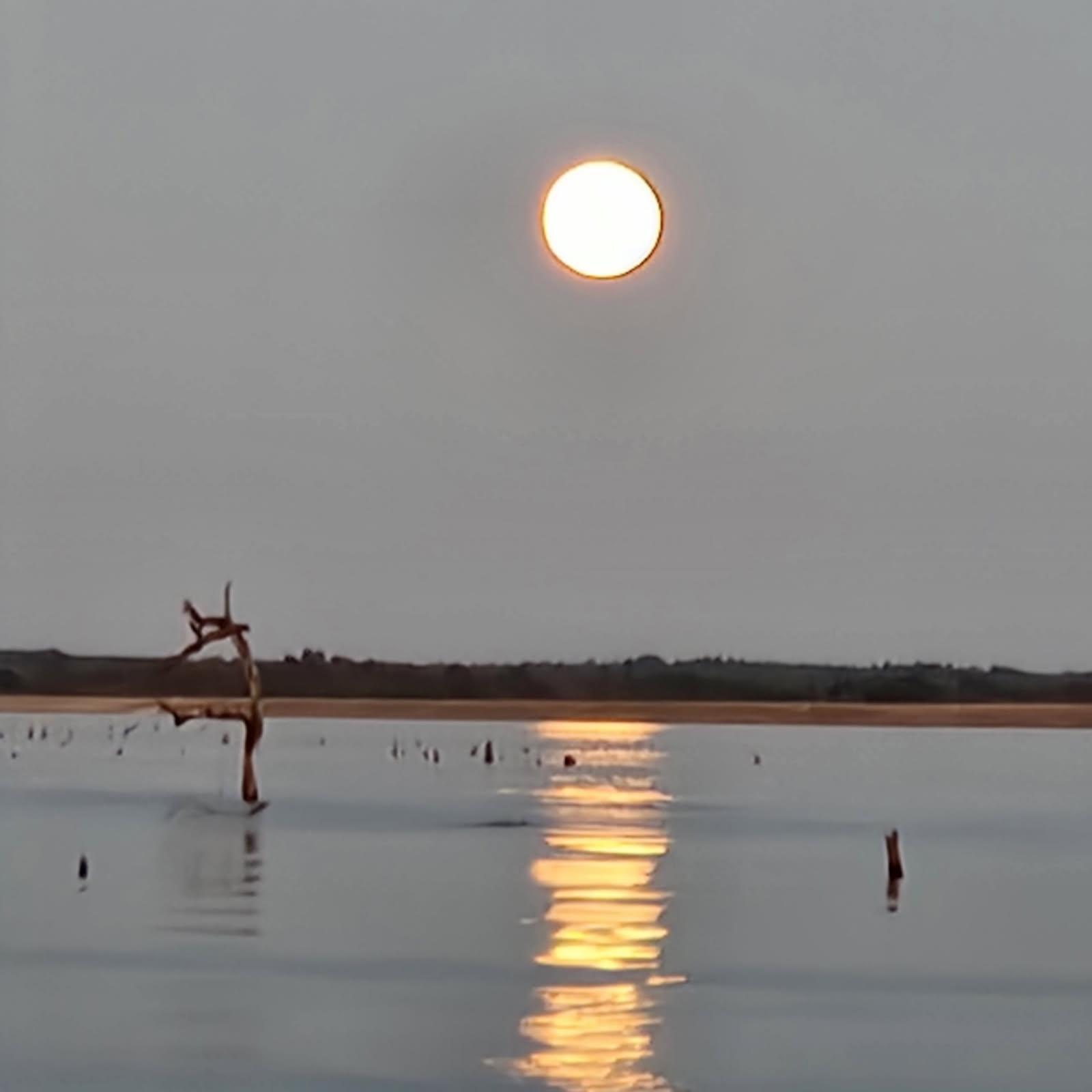 Sunset over calm lake waters in Alba TX with fishing pier and golden sun reflection