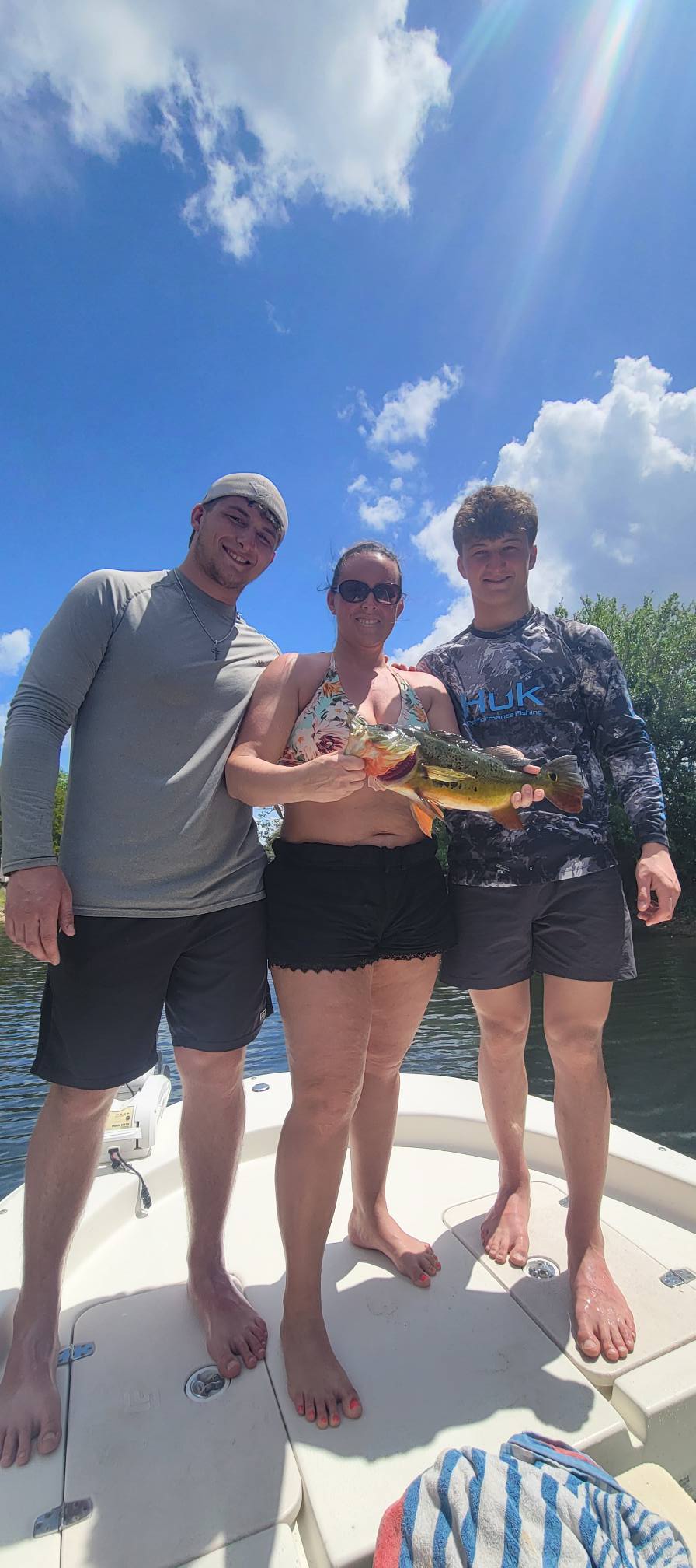 Three people on a boat holding a peacock bass after fishing in Bonita Springs FL