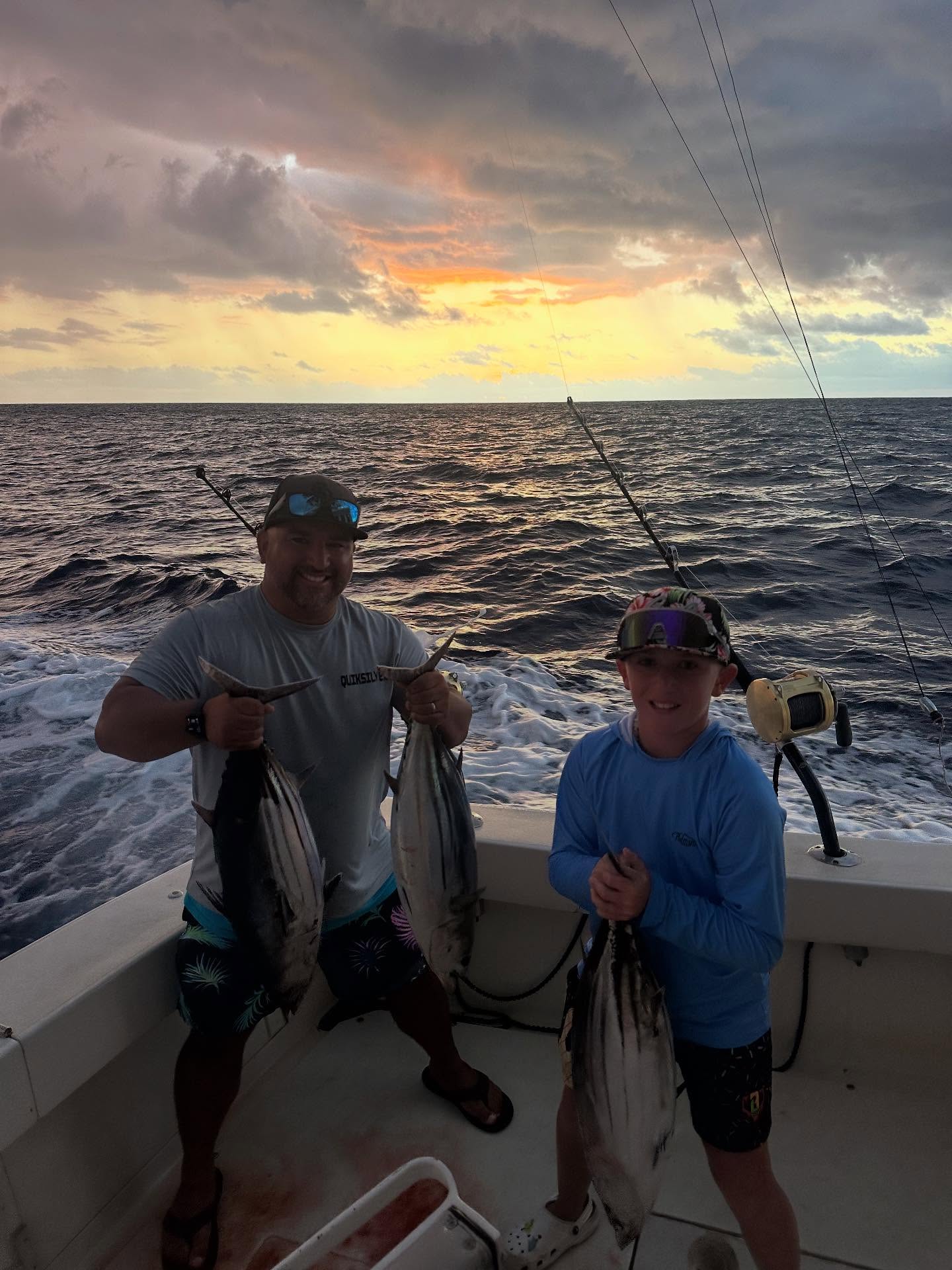 Two anglers displaying fresh caught skipjack tuna on fishing boat in Kailua-Kona Hawaii waters at sunset