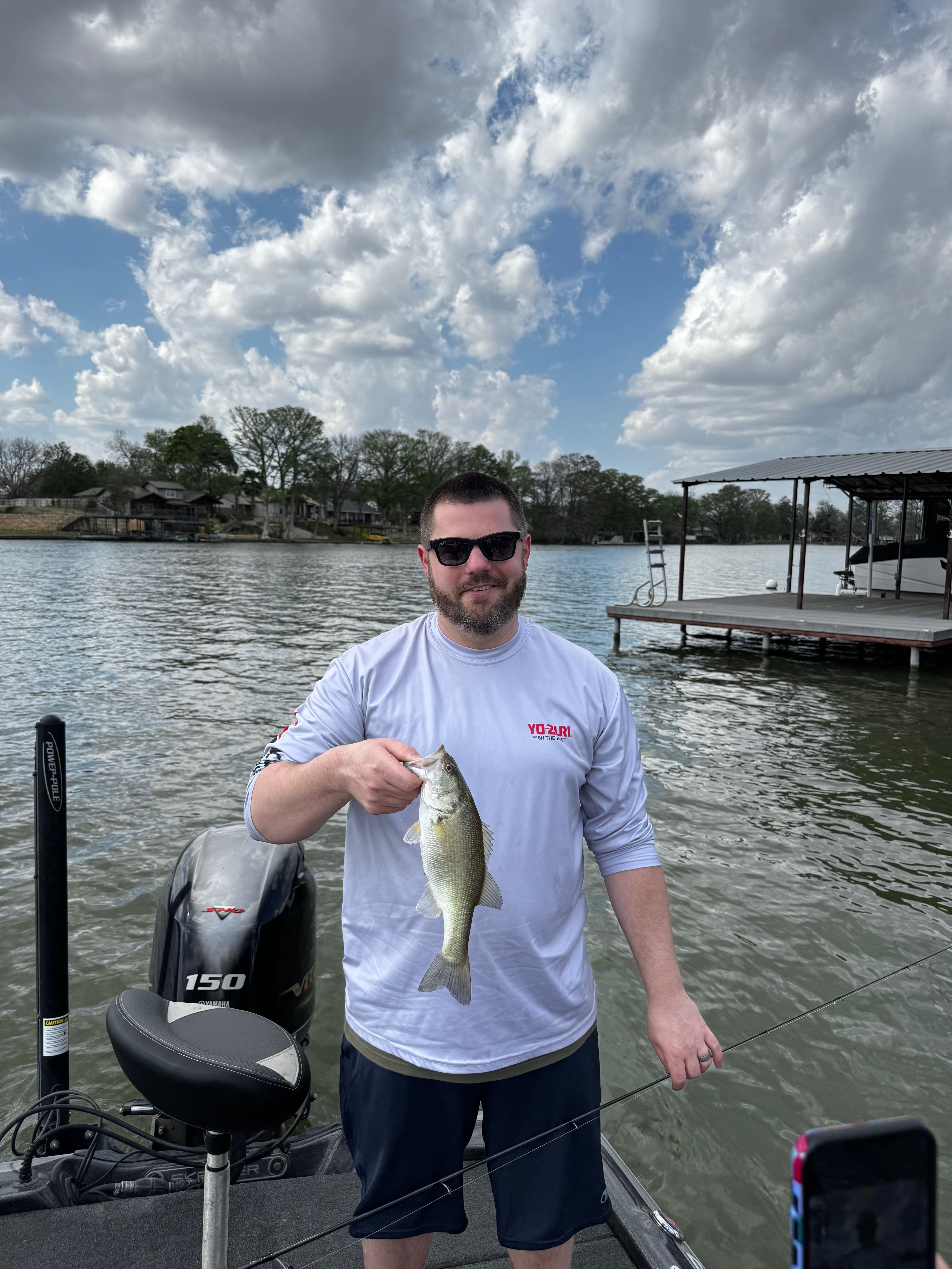 Angler holding freshly caught bass on fishing boat in New Braunfels TX lake with dock in background