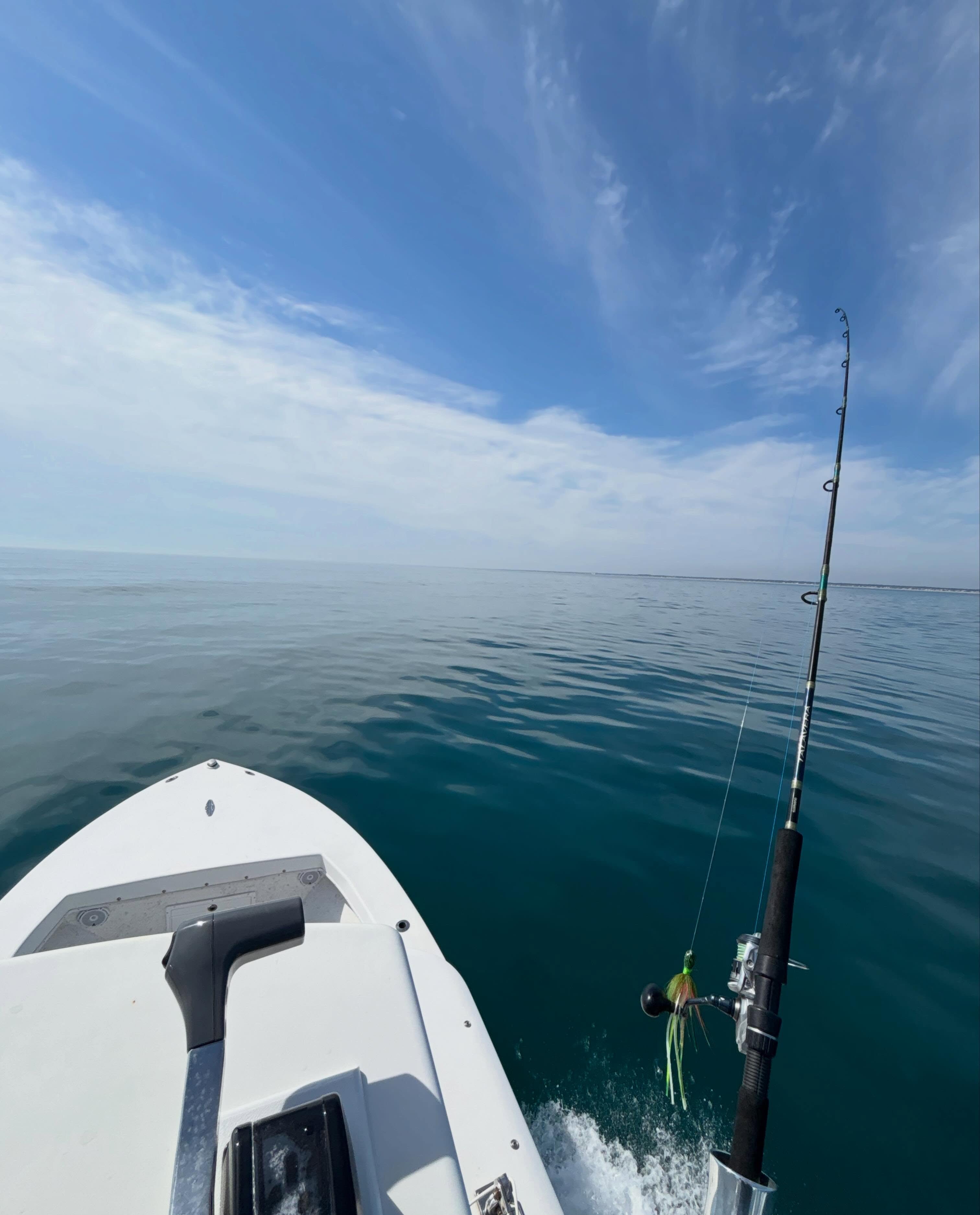 Fishing rod with green lure deployed from white boat on calm ocean waters near Virginia Beach VA