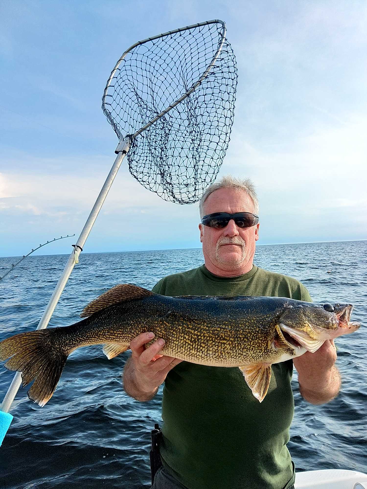 Angler holding freshly caught walleye on fishing boat in Henderson NY with landing net visible