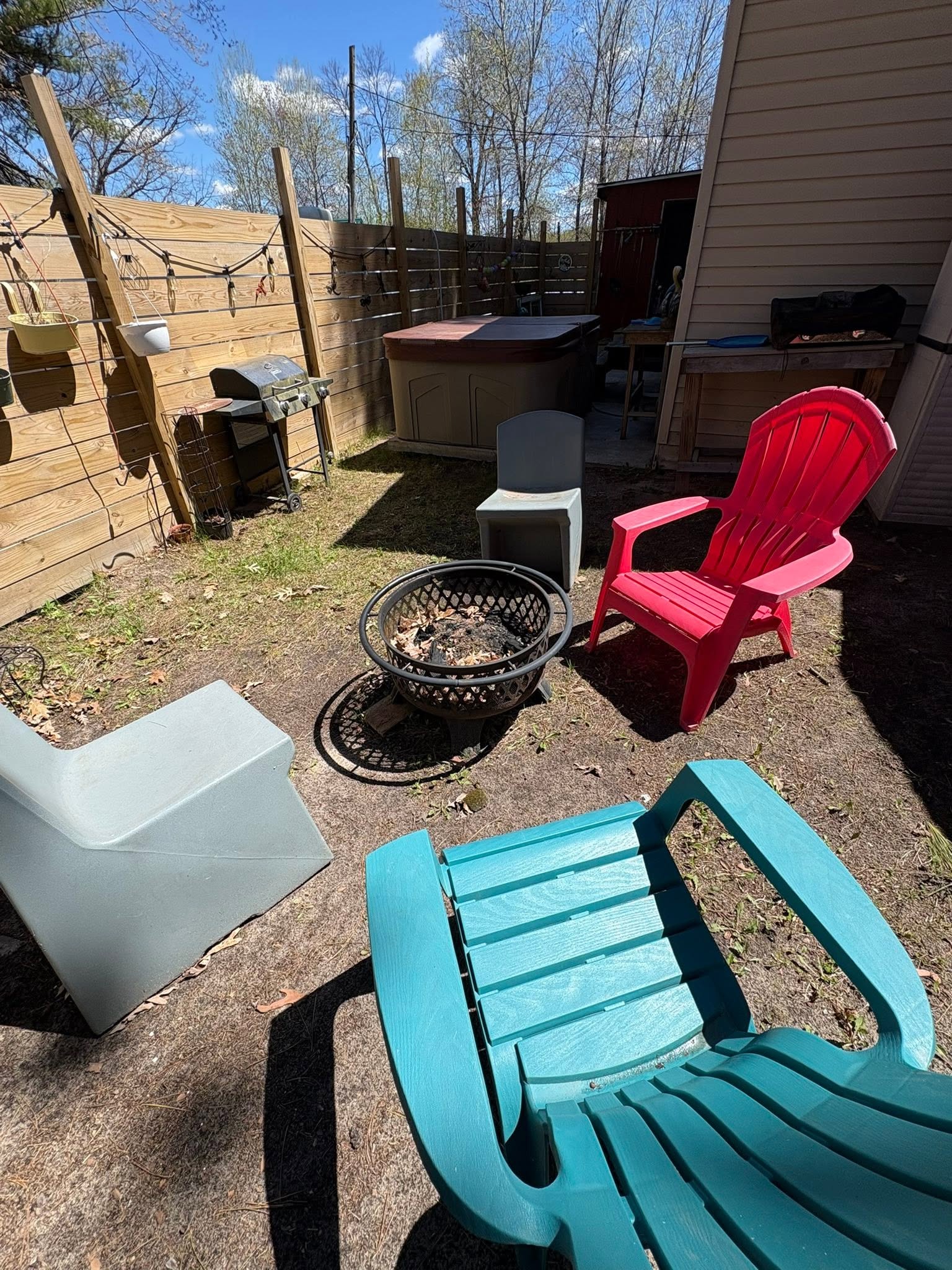 Backyard seating area with colorful plastic chairs around fire pit in Hale MI