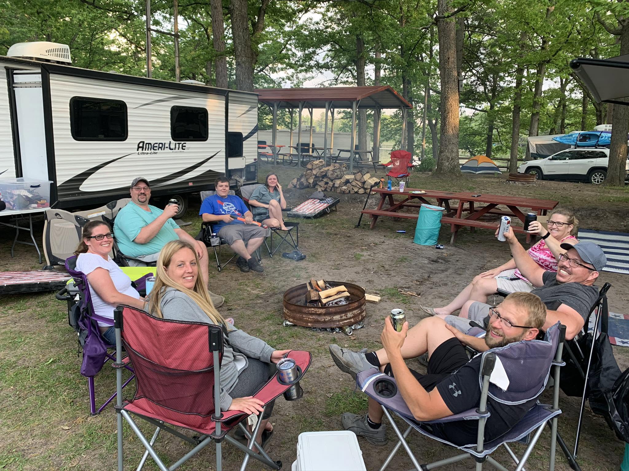 Camping scene with RV, fire pit, and chairs at campground in Hale MI