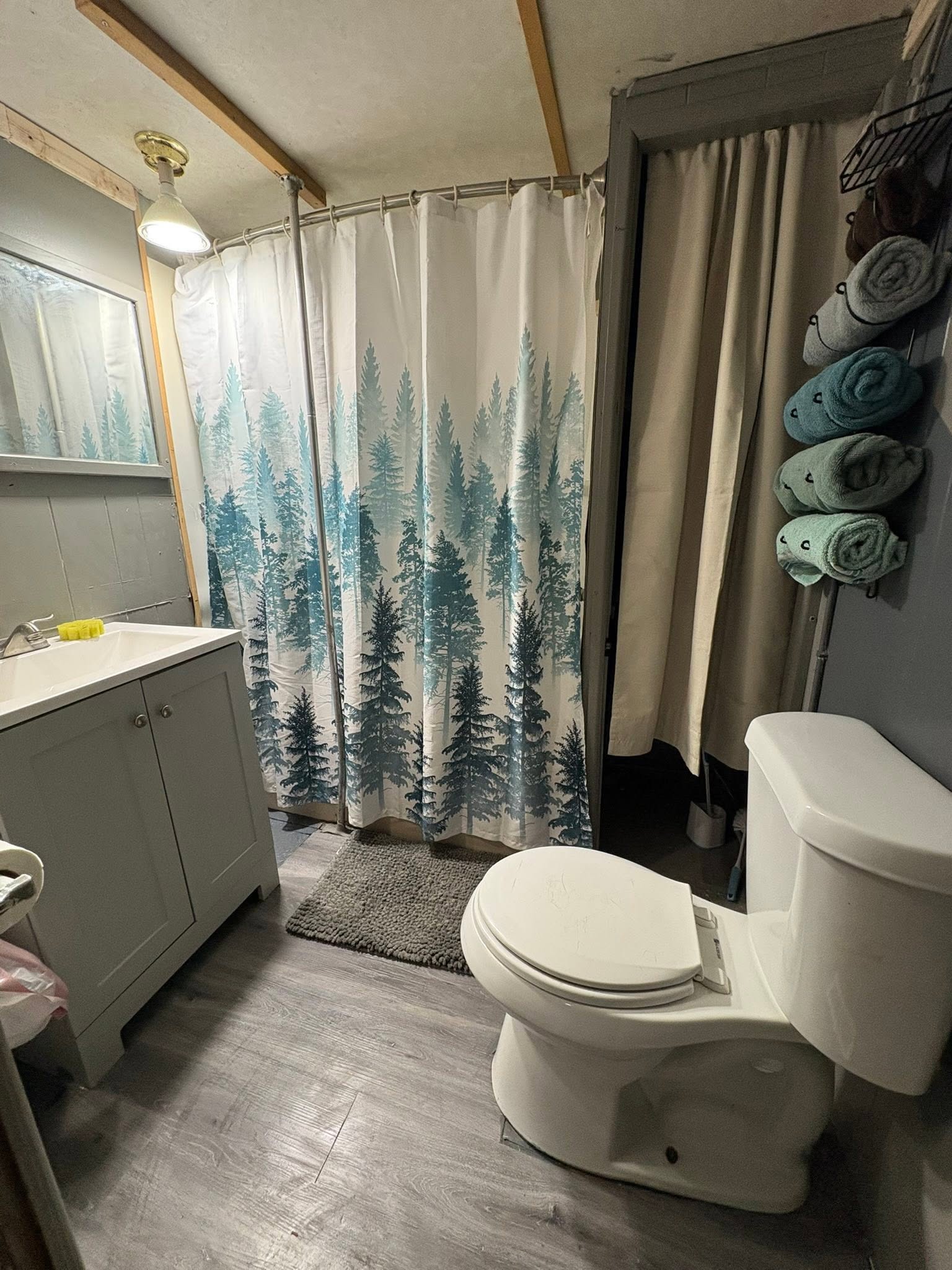 Compact RV bathroom with forest-themed shower curtain and organized towel storage in Hale MI