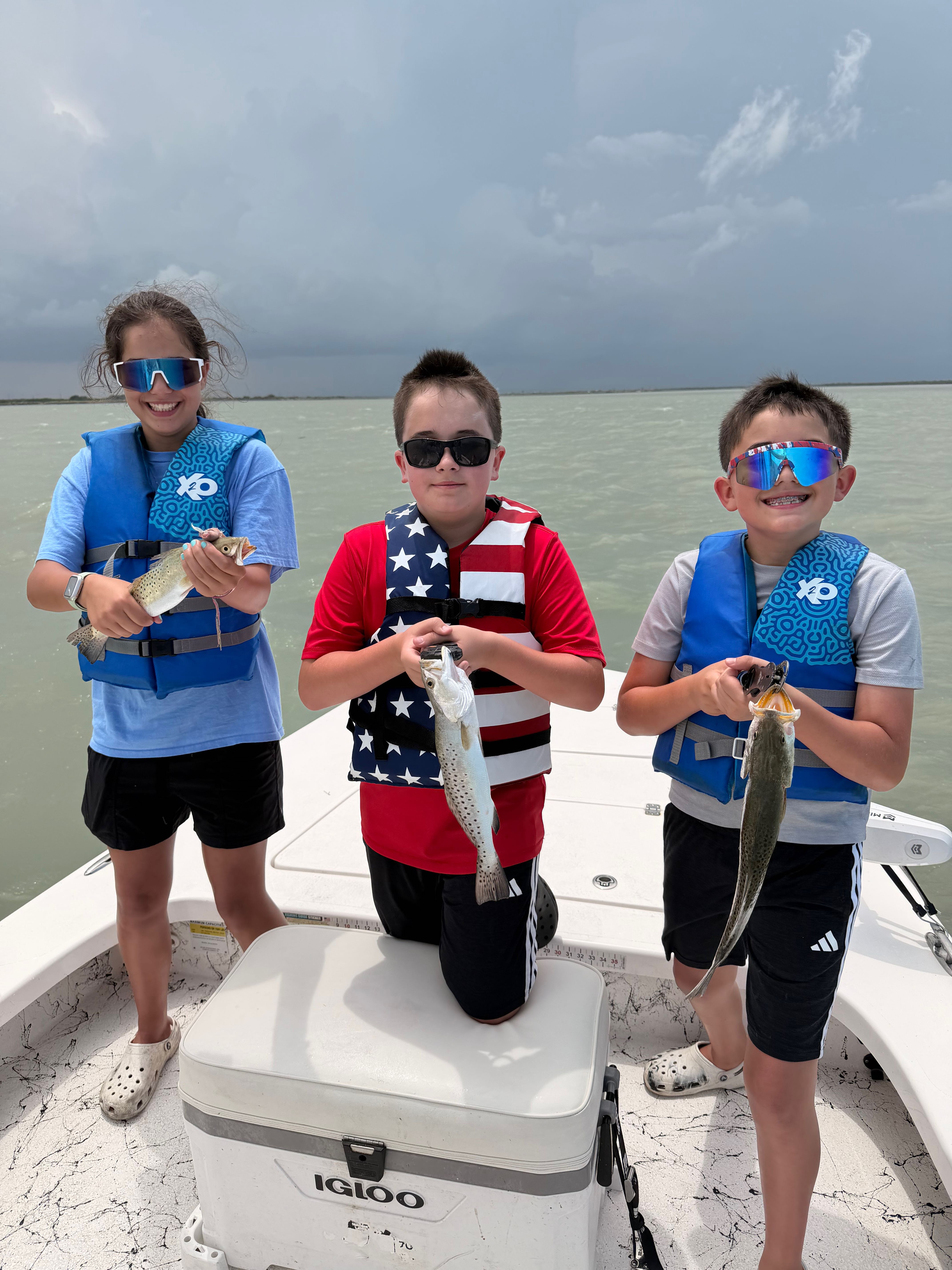 Three young anglers displaying freshly caught speckled trout on fishing boat at South Padre Island TX