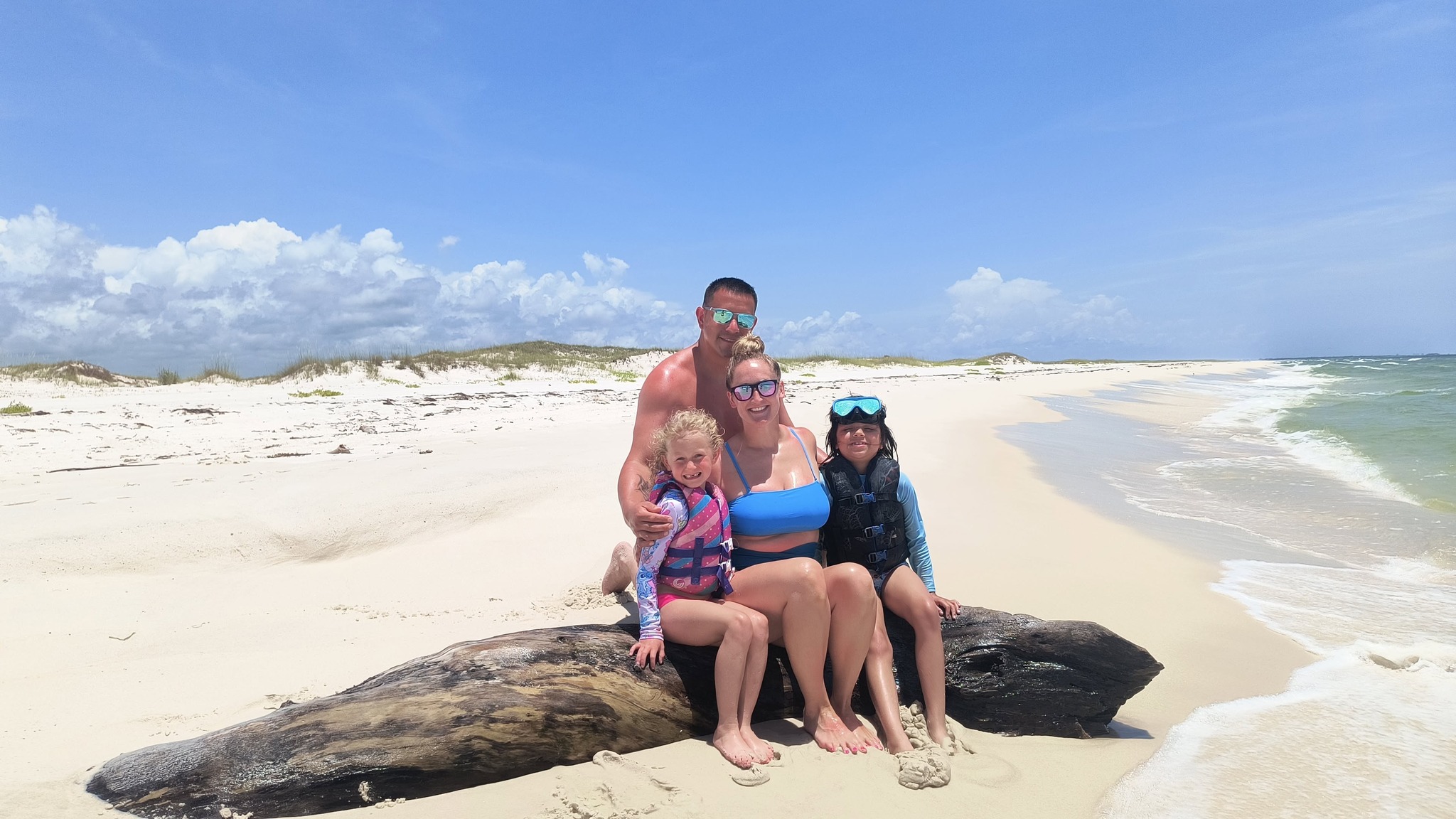 Family enjoying beach time on driftwood log in Orange Beach AL
