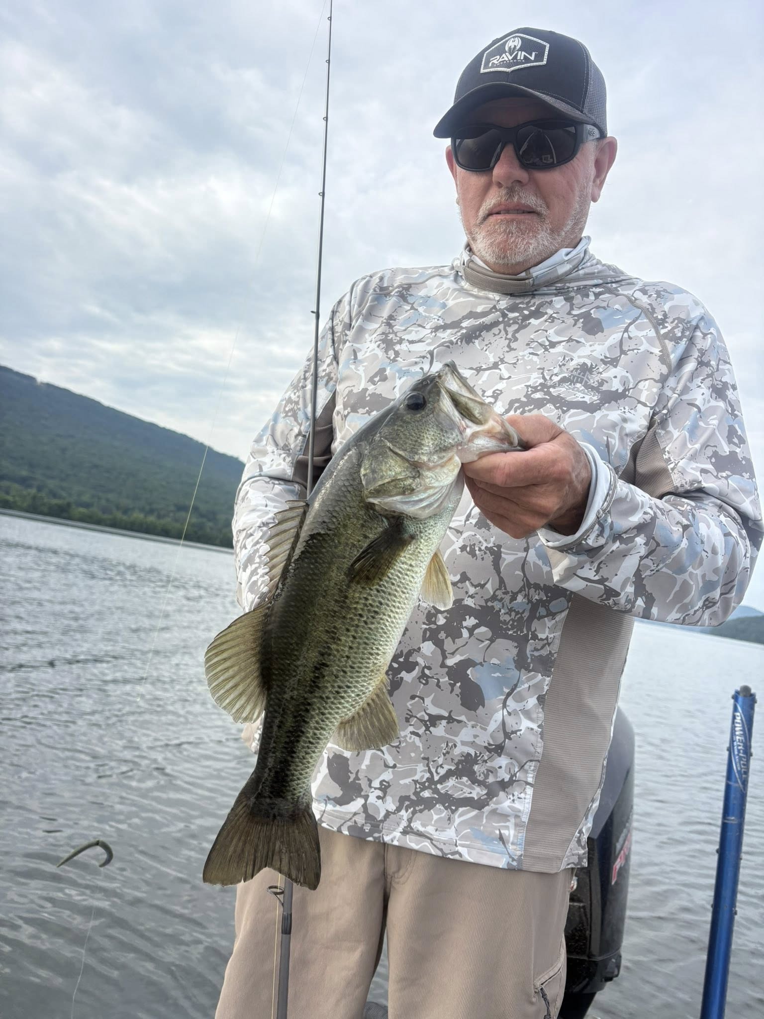 Angler holding caught bass on boat in Chattanooga TN lake with fishing rod and mountains in background