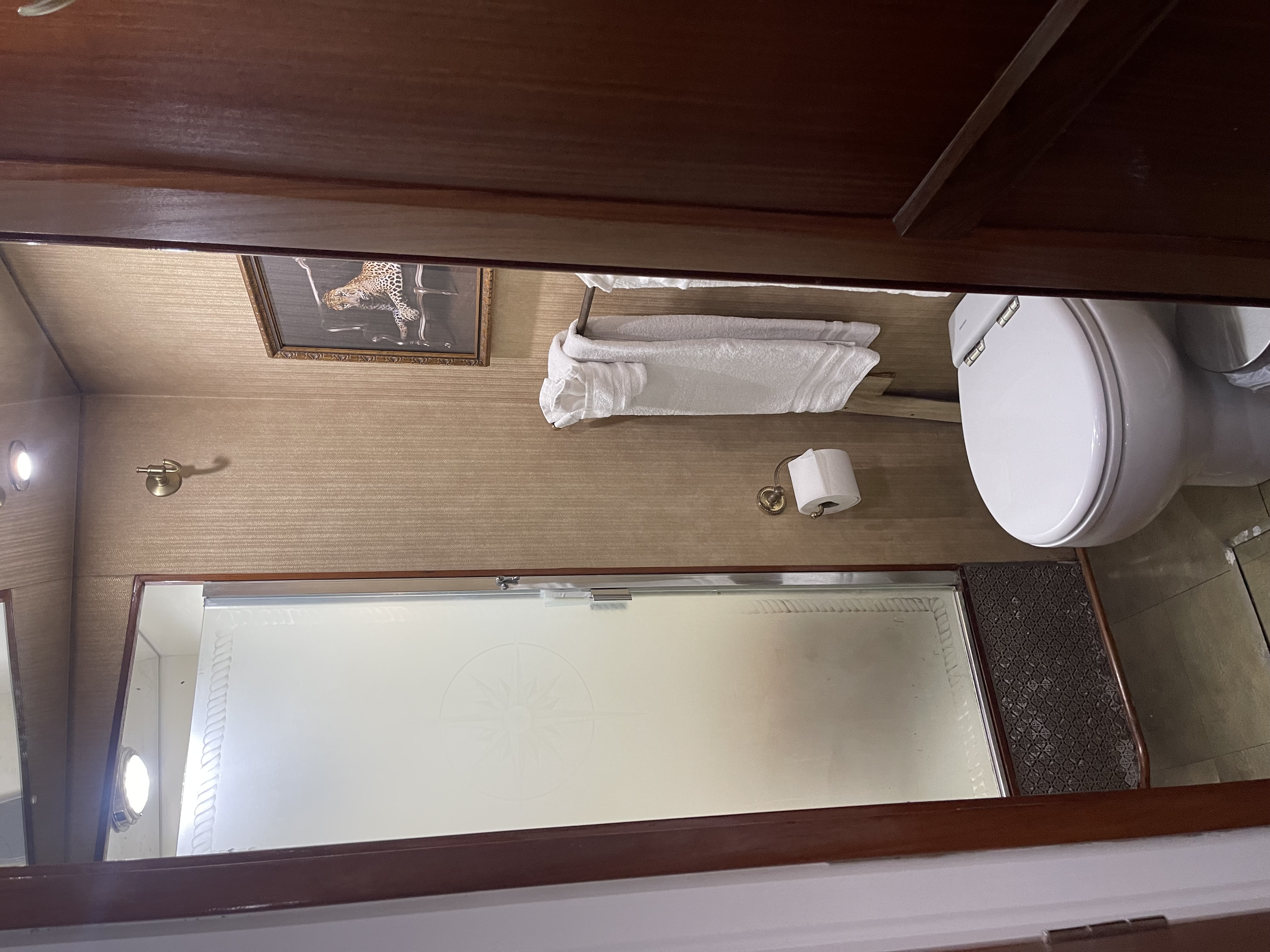 Compact bathroom interior aboard a fishing charter vessel in San Diego CA with white toilet, towel rack, and mirror