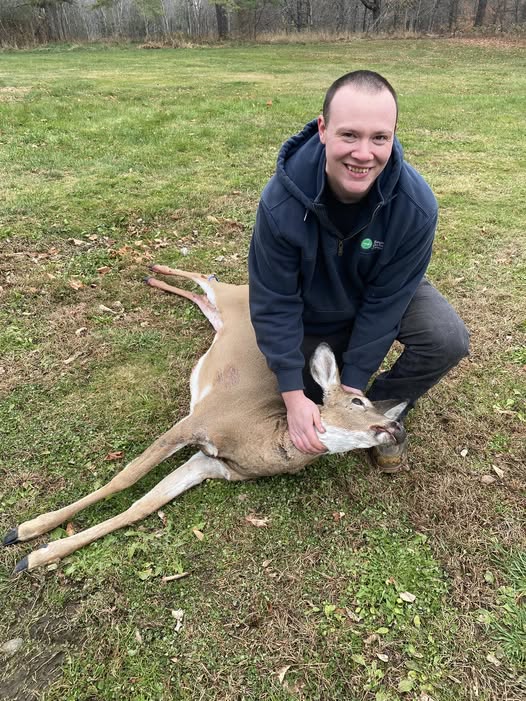 Hunter with harvested deer on grassy field in Harmony ME