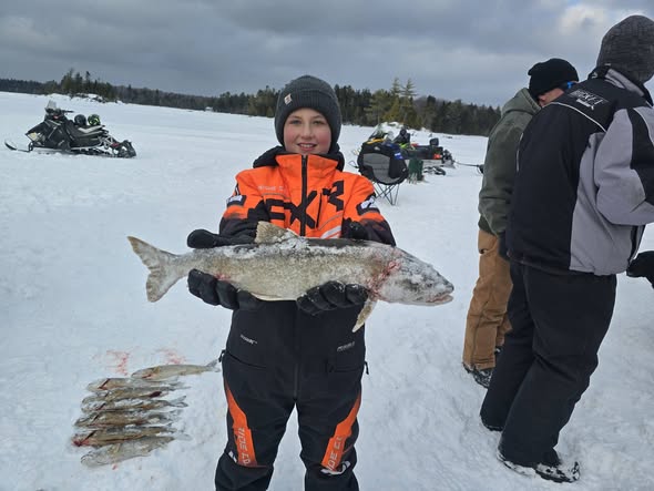 Ice fishing scene in Harmony ME showing fresh caught fish on snowy surface with snowmobiles in background