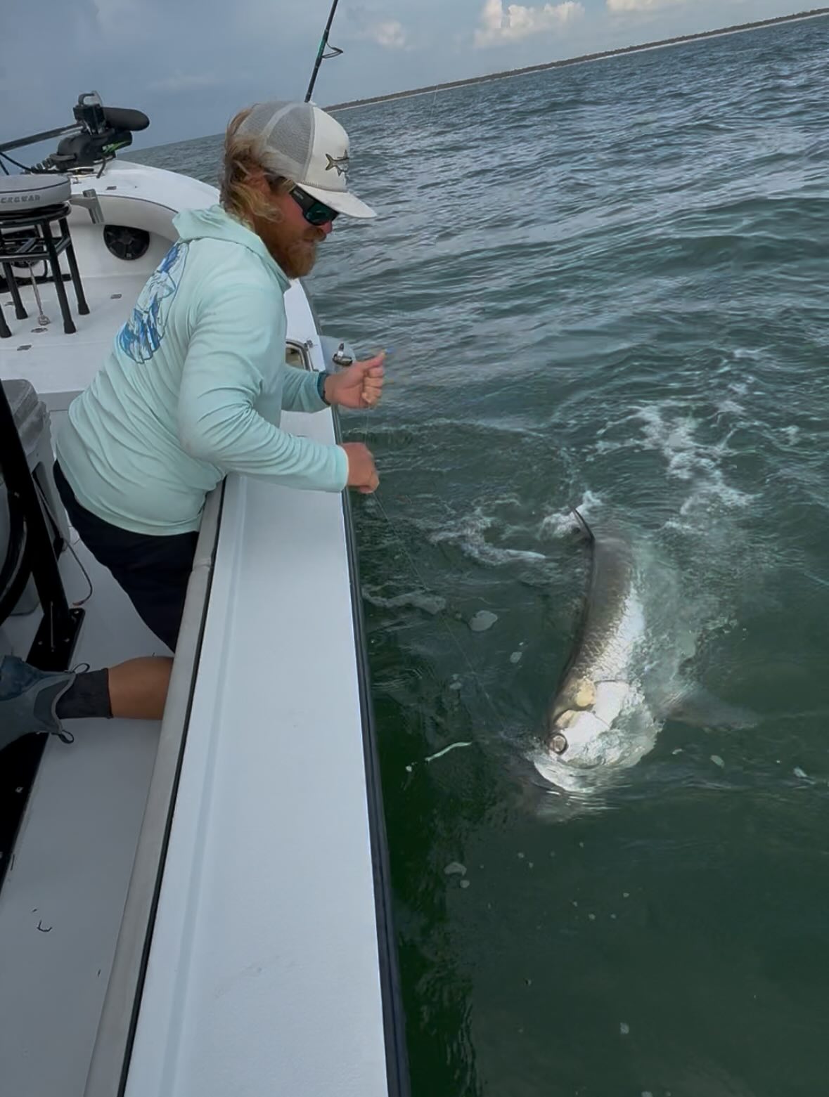 Tarpon jumping and splashing in green ocean water next to fishing boat in Placida FL