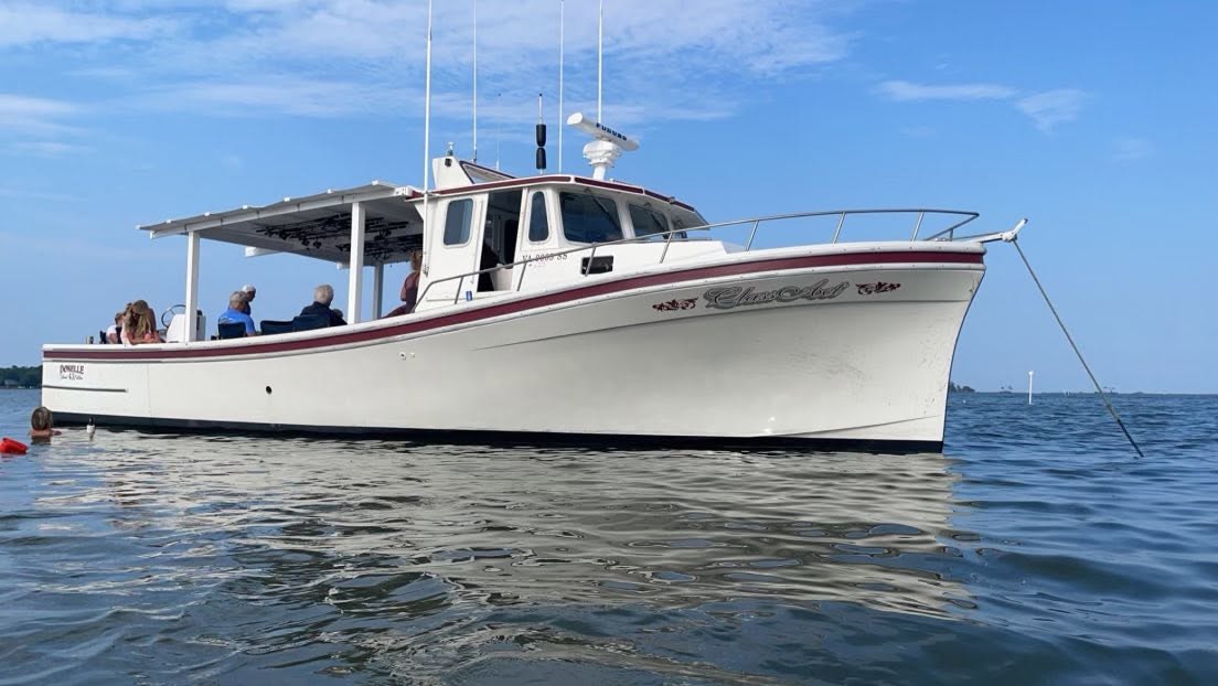 White fishing boat anchored on calm water near Gwynn Island VA with passengers aboard