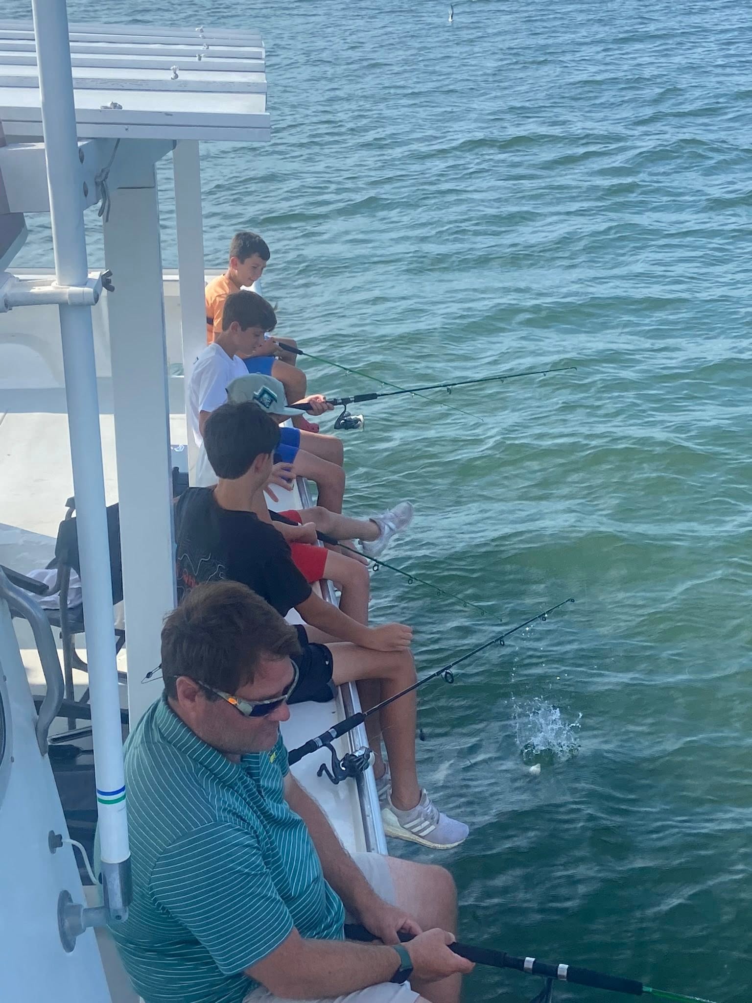 Multiple fishing rods cast from white boat deck into green ocean waters near Gwynn Island VA