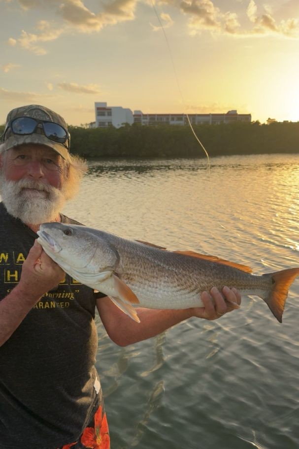 Redfish catch held over water in Indian Shores FL at sunset