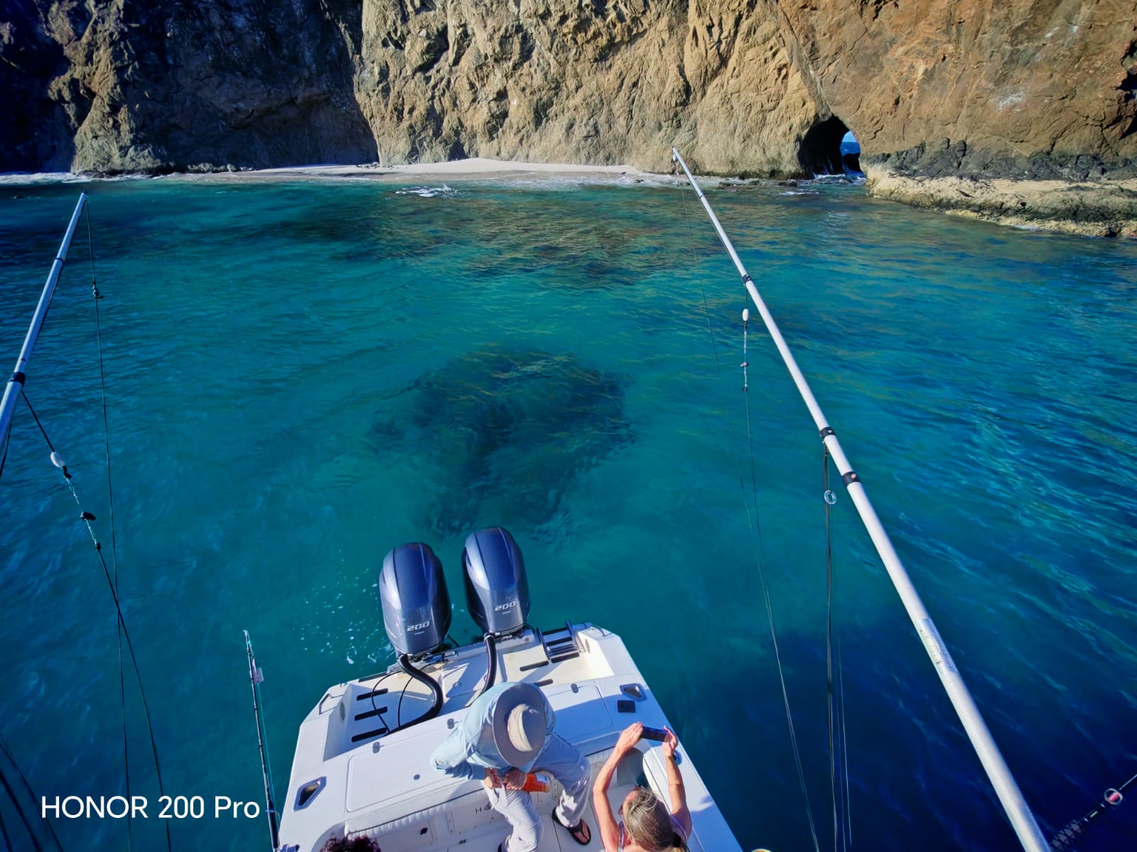 Fishing boat with twin outboard motors anchored in crystal clear turquoise waters near dramatic rocky cliffs in Guanacaste