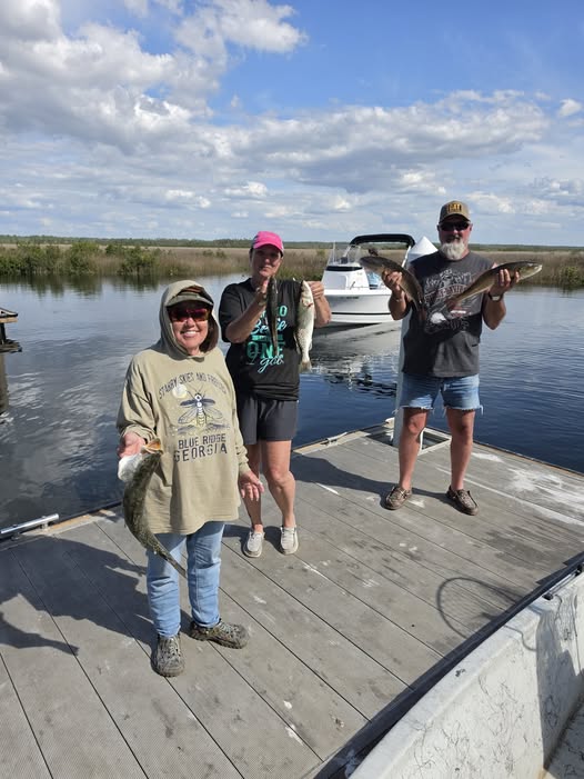 Three anglers displaying their catch on wooden dock in Spring Hill FL with boat in background