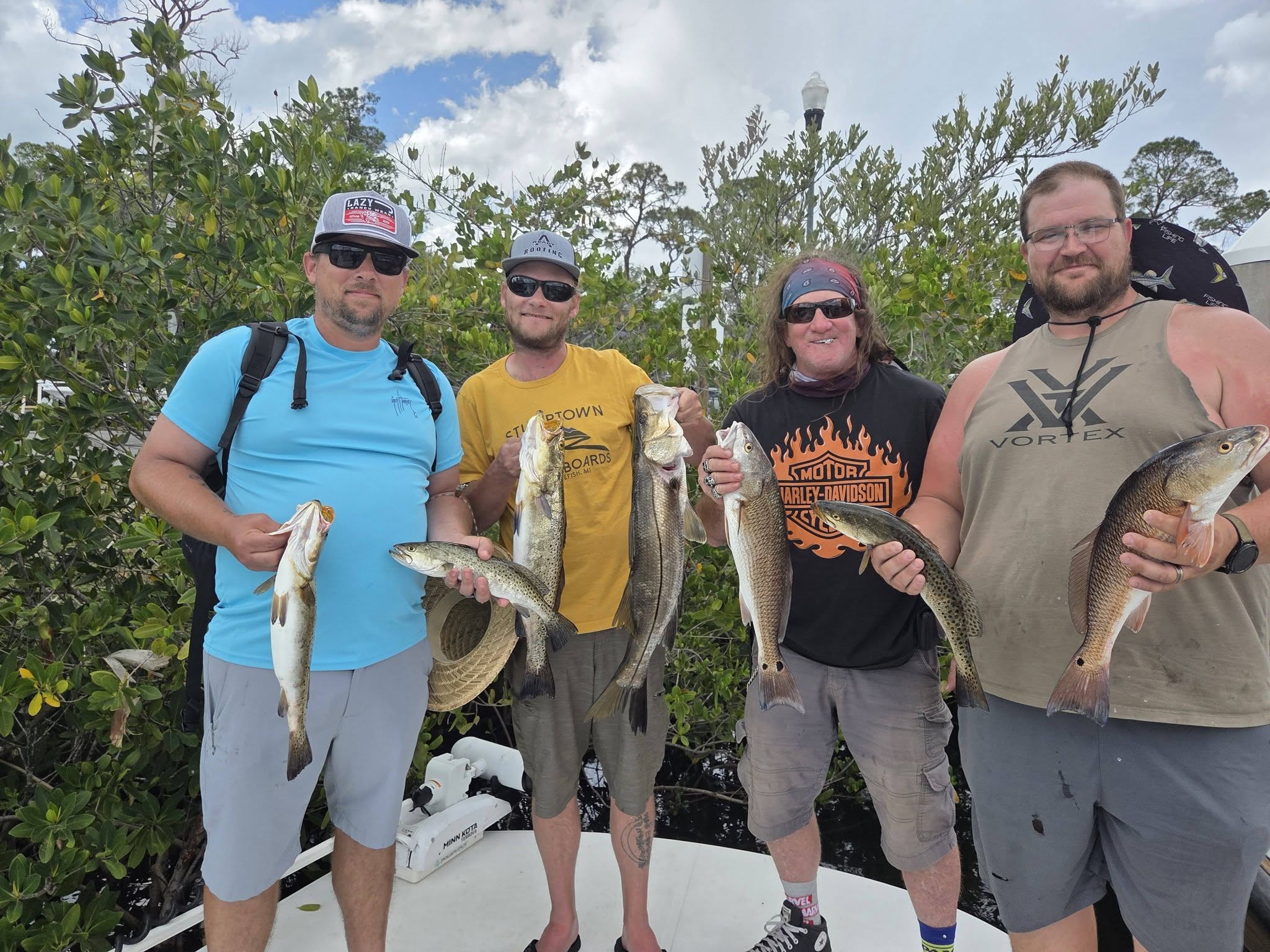 Four anglers displaying freshly caught redfish, speckled trout, and snook from Bayport FL fishing trip
