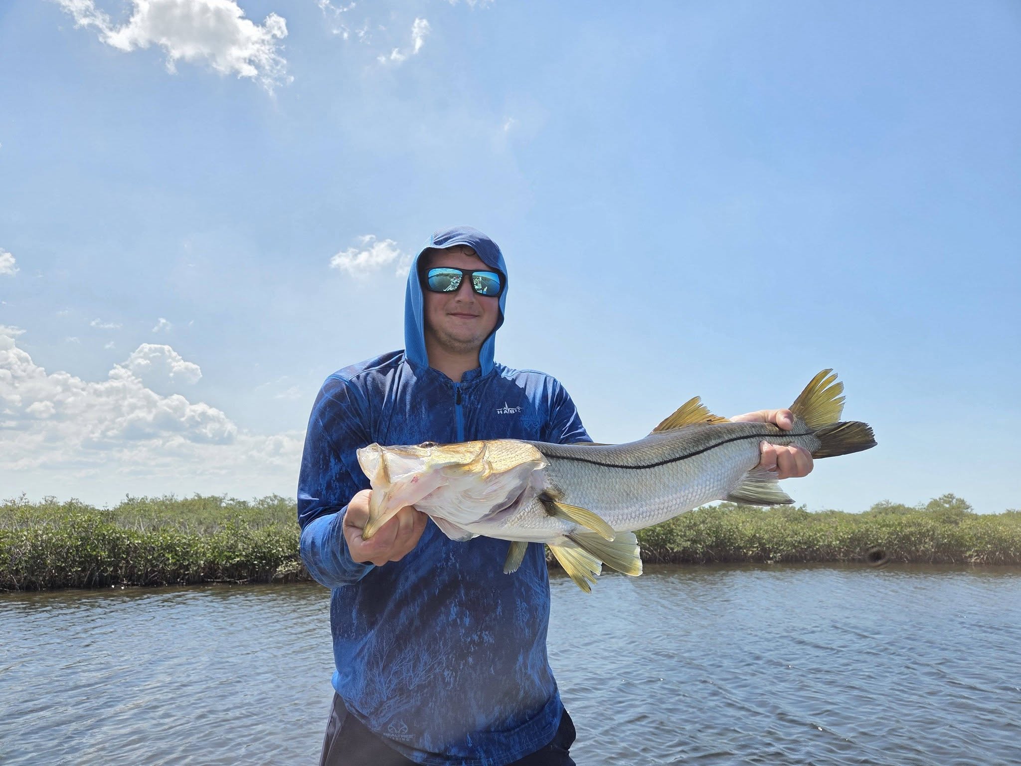 Angler holding caught snook in Bayport FL waters with mangroves in background