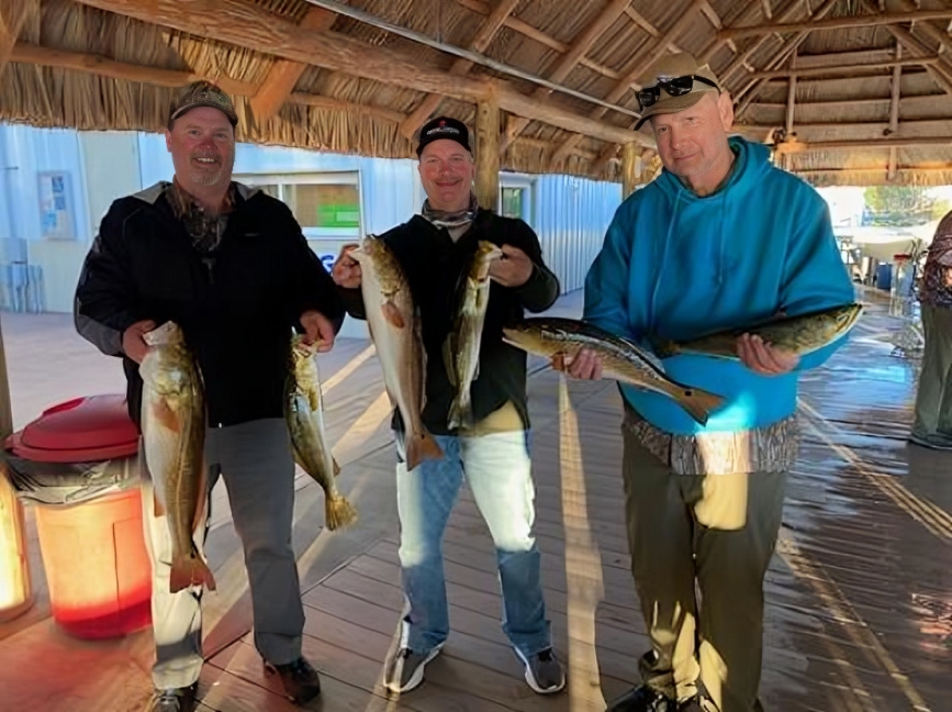 Three anglers displaying freshly caught redfish under covered dock area in Steinhatchee FL
