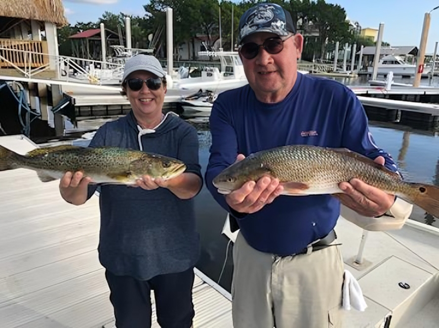 Two anglers displaying freshly caught redfish and speckled trout on fishing boat in Steinhatchee FL marina