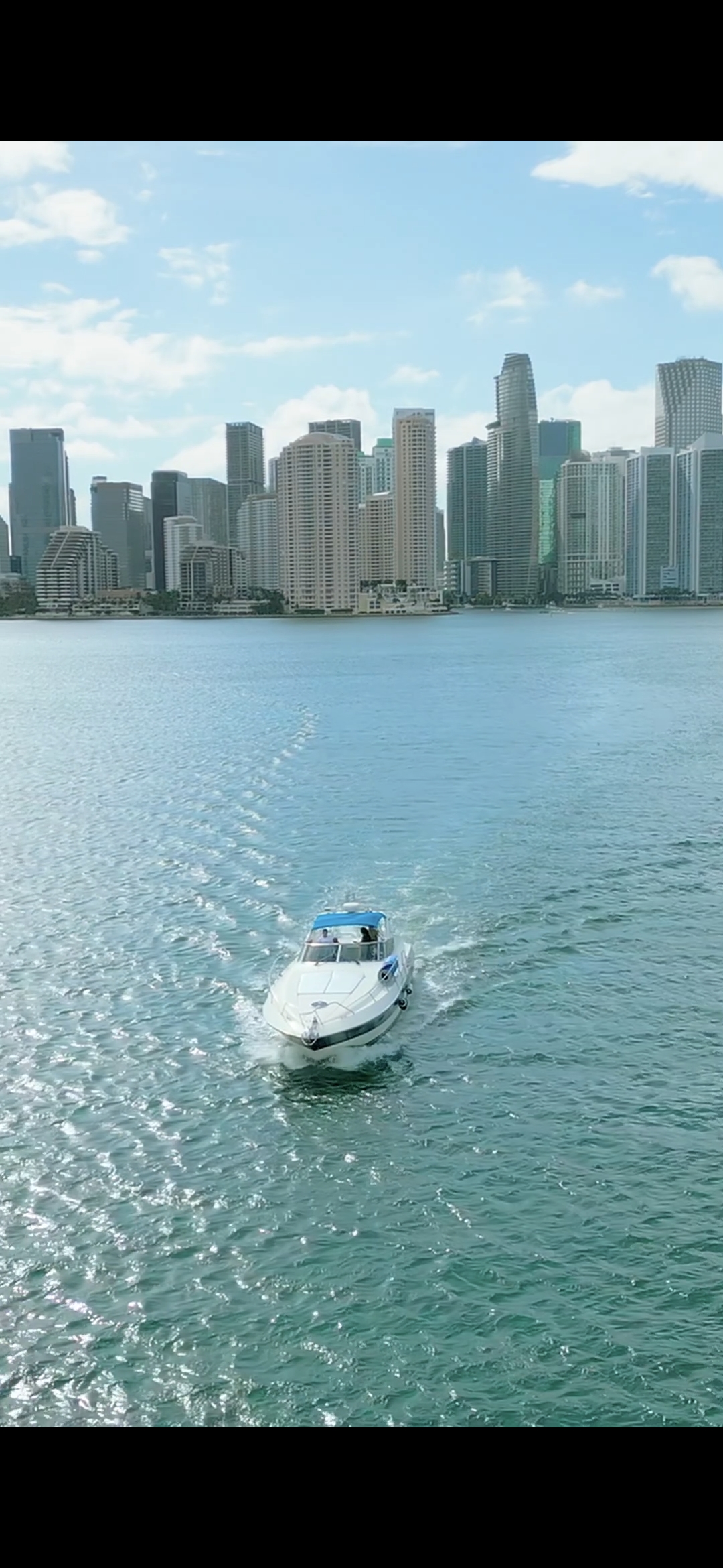 White speedboat cruising through turquoise waters with Miami FL skyline in background