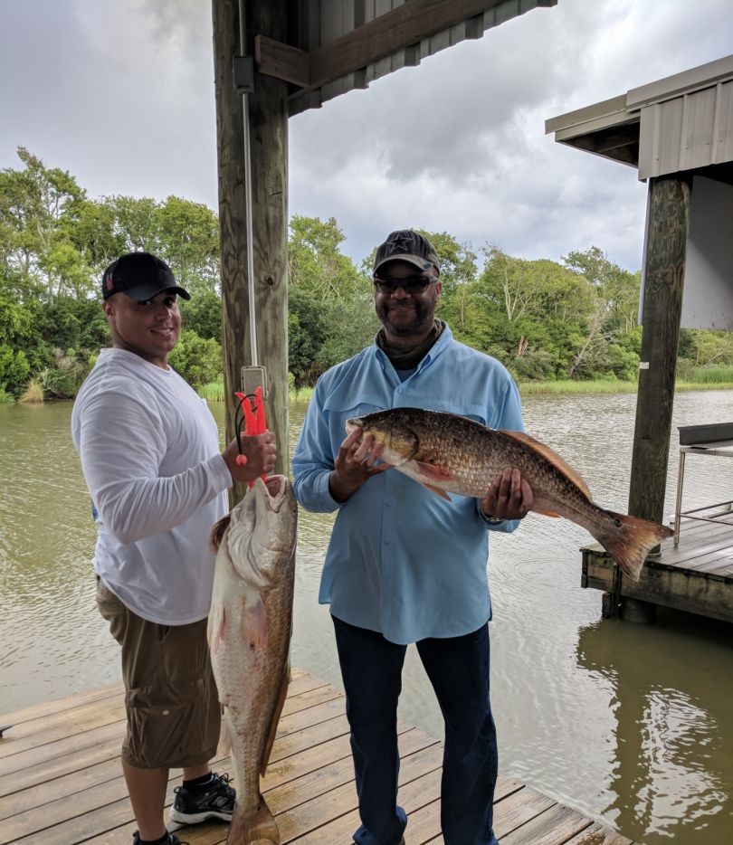 Two anglers displaying caught redfish on wooden dock in Theriot Louisiana