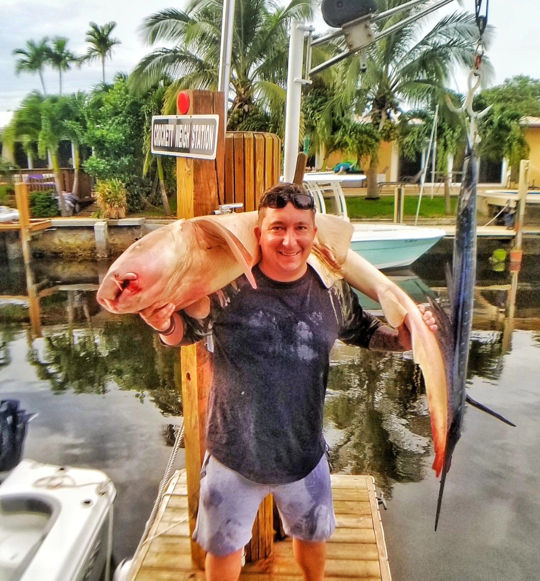Large fish catch displayed at fishing dock in Pompano Beach FL with tropical palm trees and boats in background