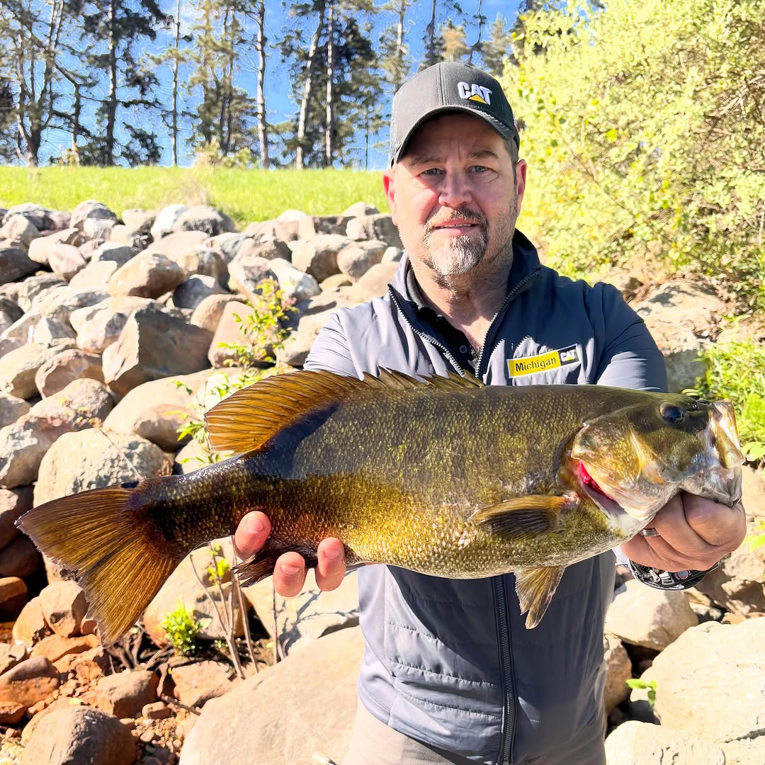 Smallmouth bass catch in Stanwood MI with rocky shoreline and trees in background