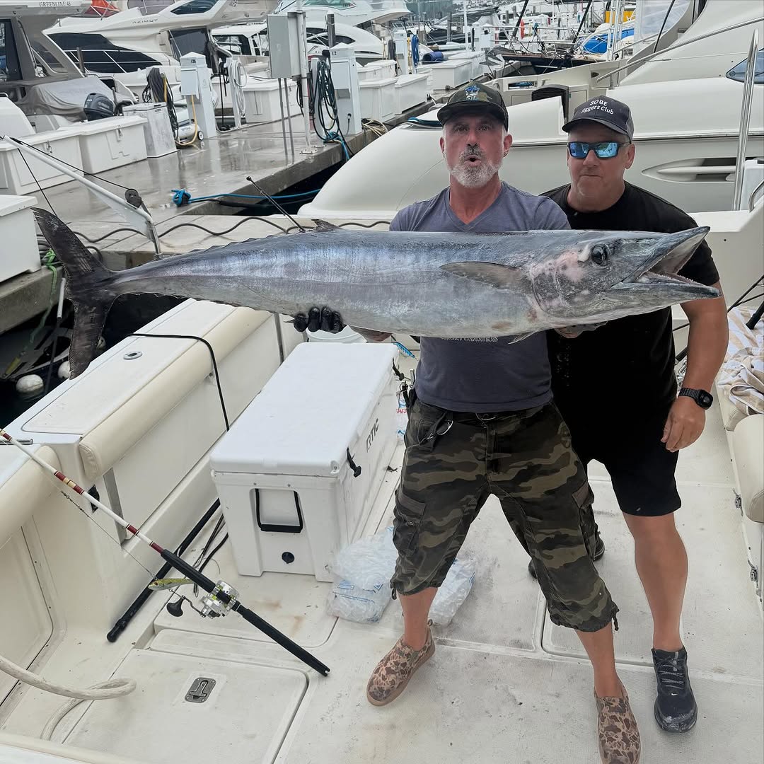 Two anglers holding large wahoo fish on boat deck at marina in New York City