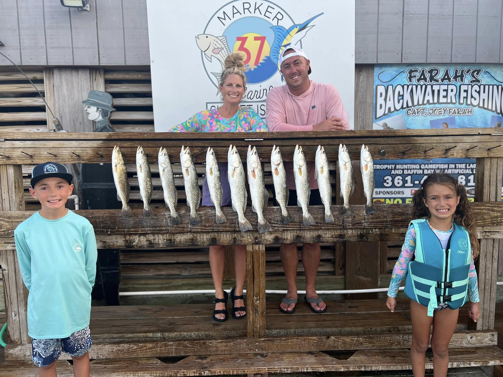 Twelve speckled trout displayed on wooden dock railing at fishing charter in Corpus Christi TX