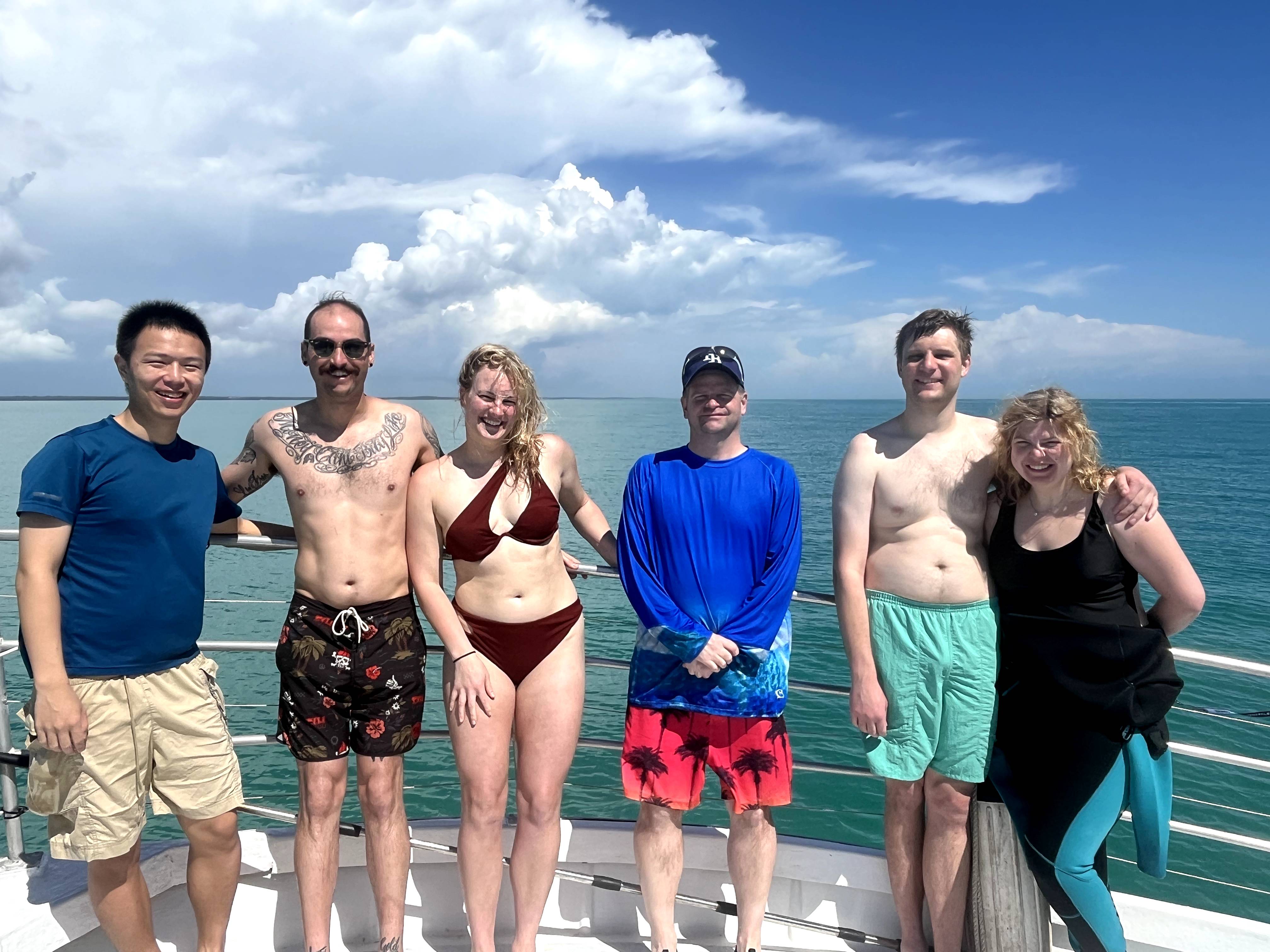 Group of six people on boat deck with ocean and cloudy sky in background