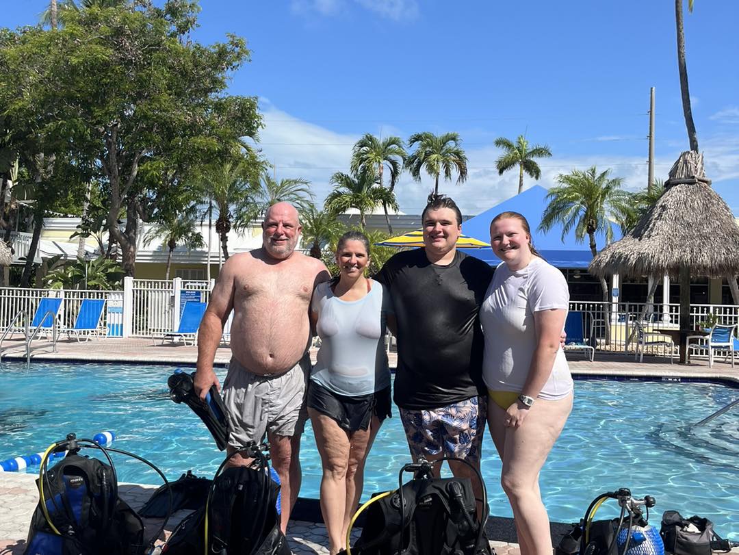 Scuba diving group with equipment poolside at tropical resort with palm trees