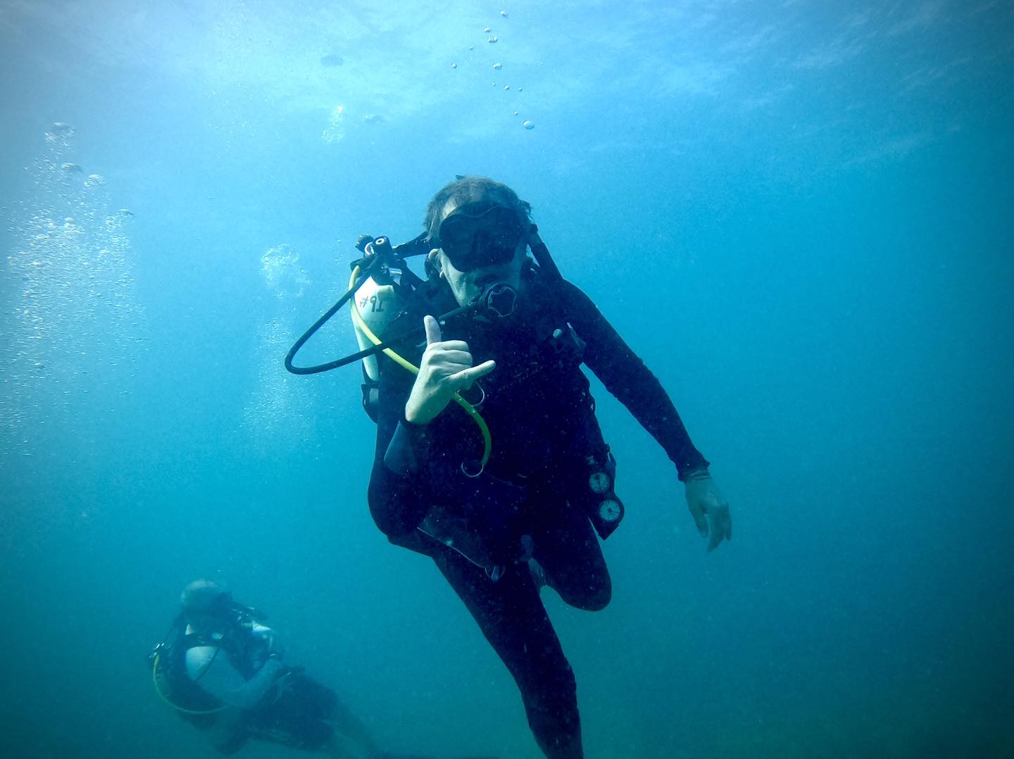 Scuba diver swimming underwater giving thumbs up signal with another diver visible in background