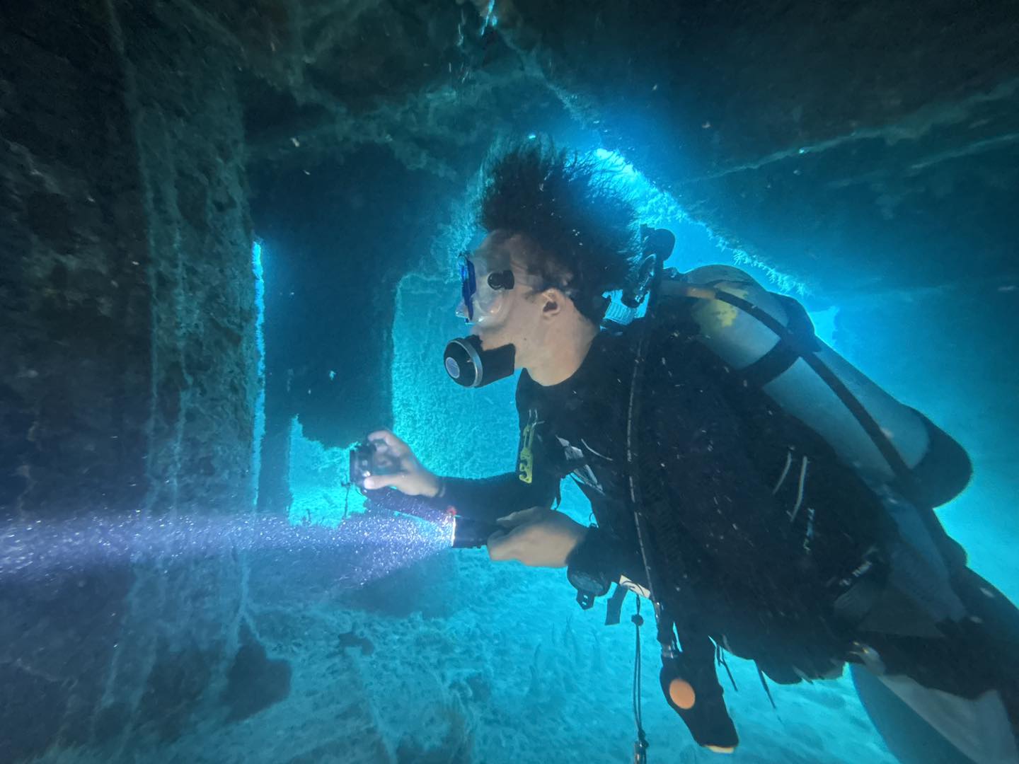 Underwater scuba diving scene showing diver using drilling equipment on shipwreck structure in blue water