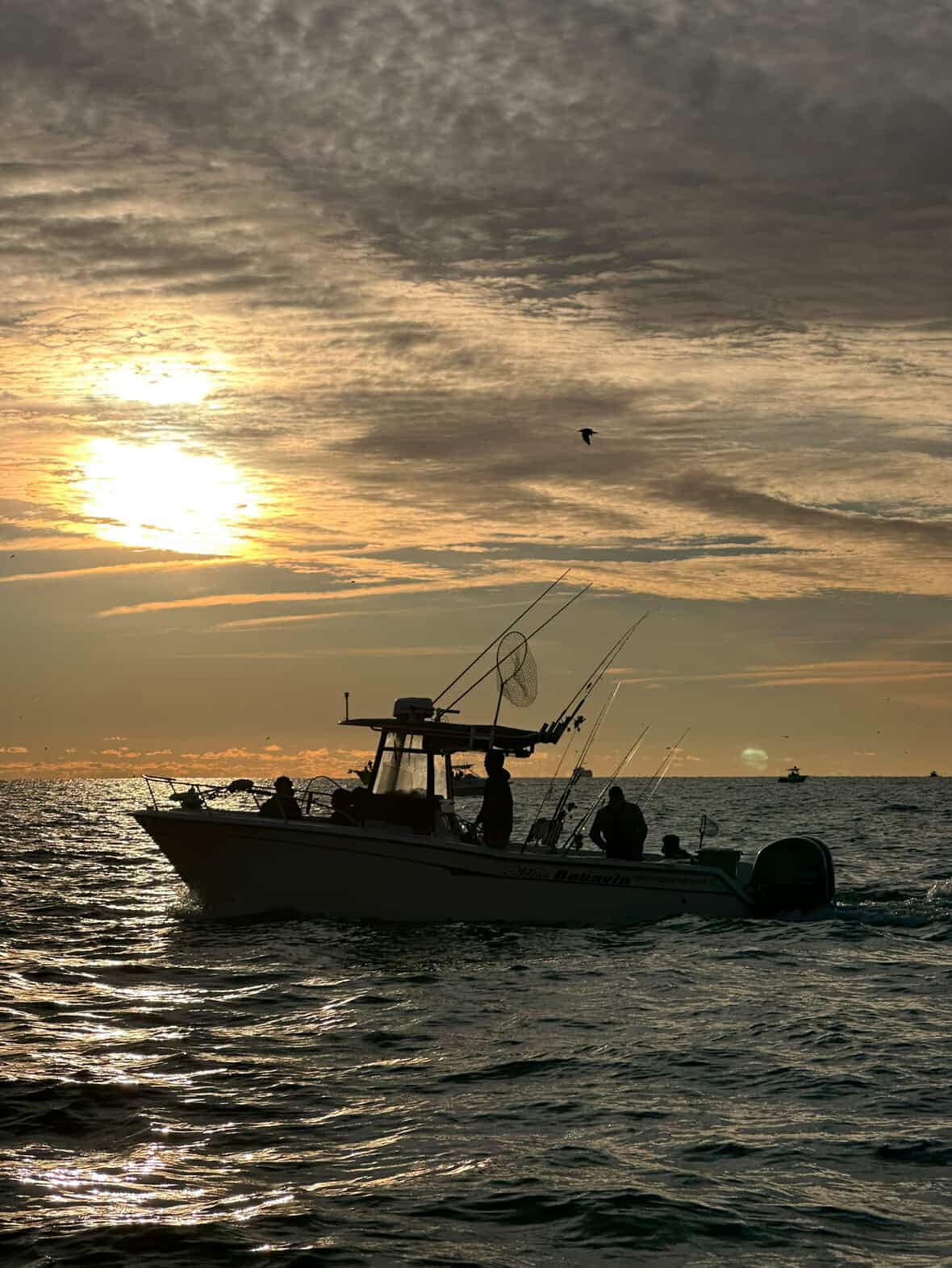 Fishing boat with multiple rods silhouetted against golden sunset sky on ocean waters near Woodbridge Township NJ