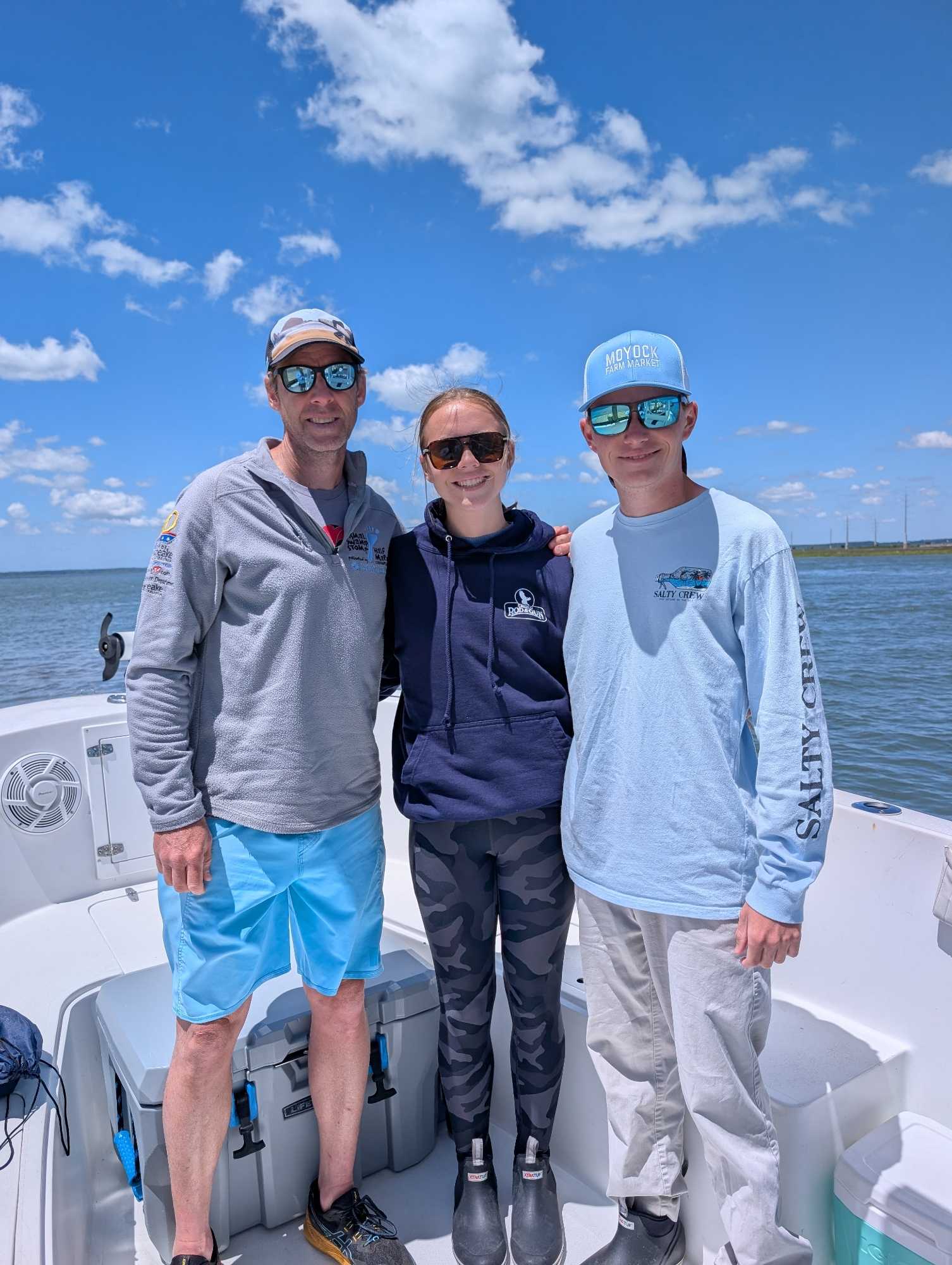 Three people posing together on a fishing boat in Chincoteague VA waters under blue sky with white clouds
