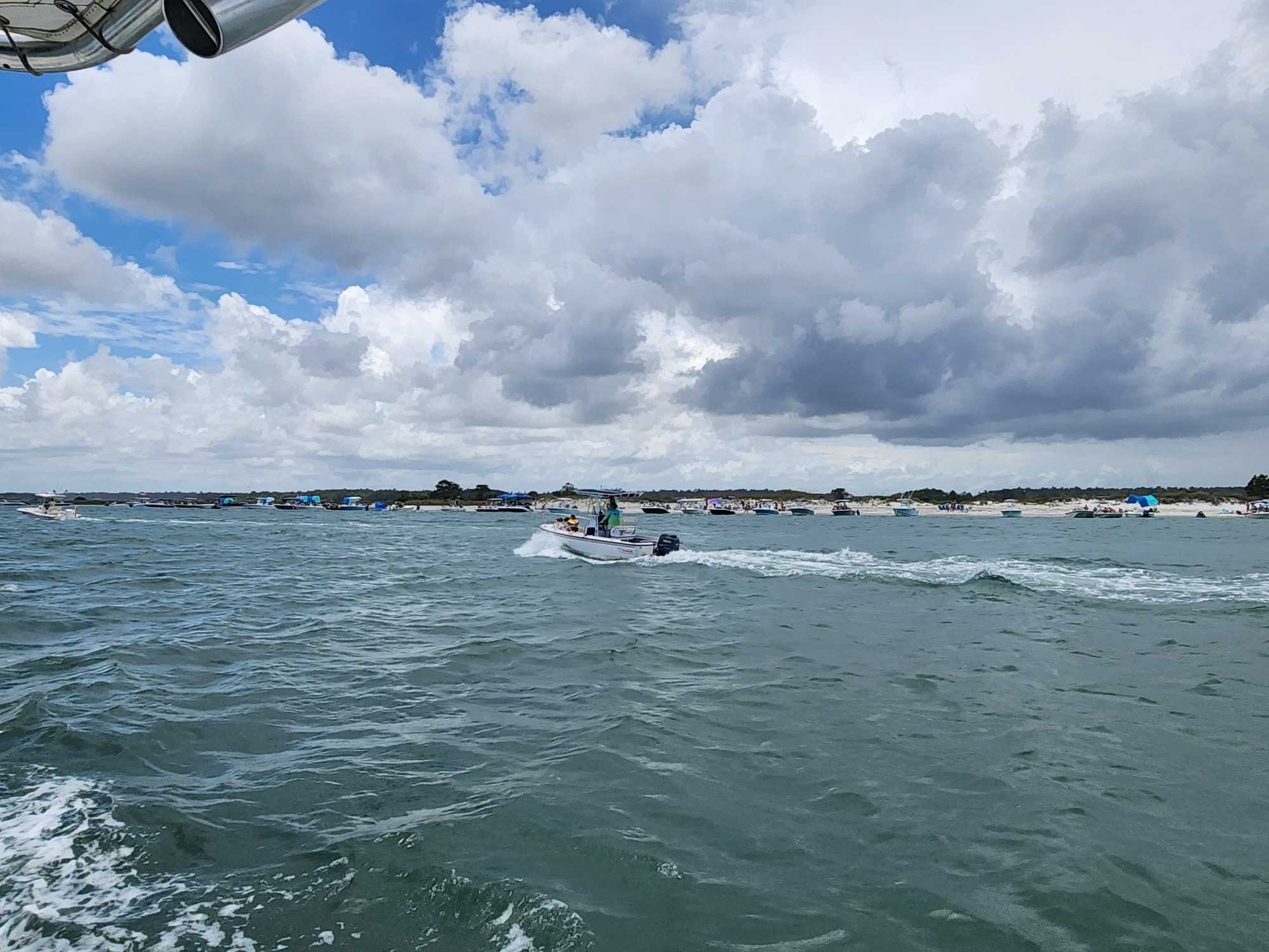 Boat cruising through choppy green waters near Carolina Beach NC with multiple boats anchored in background under cloudy sky