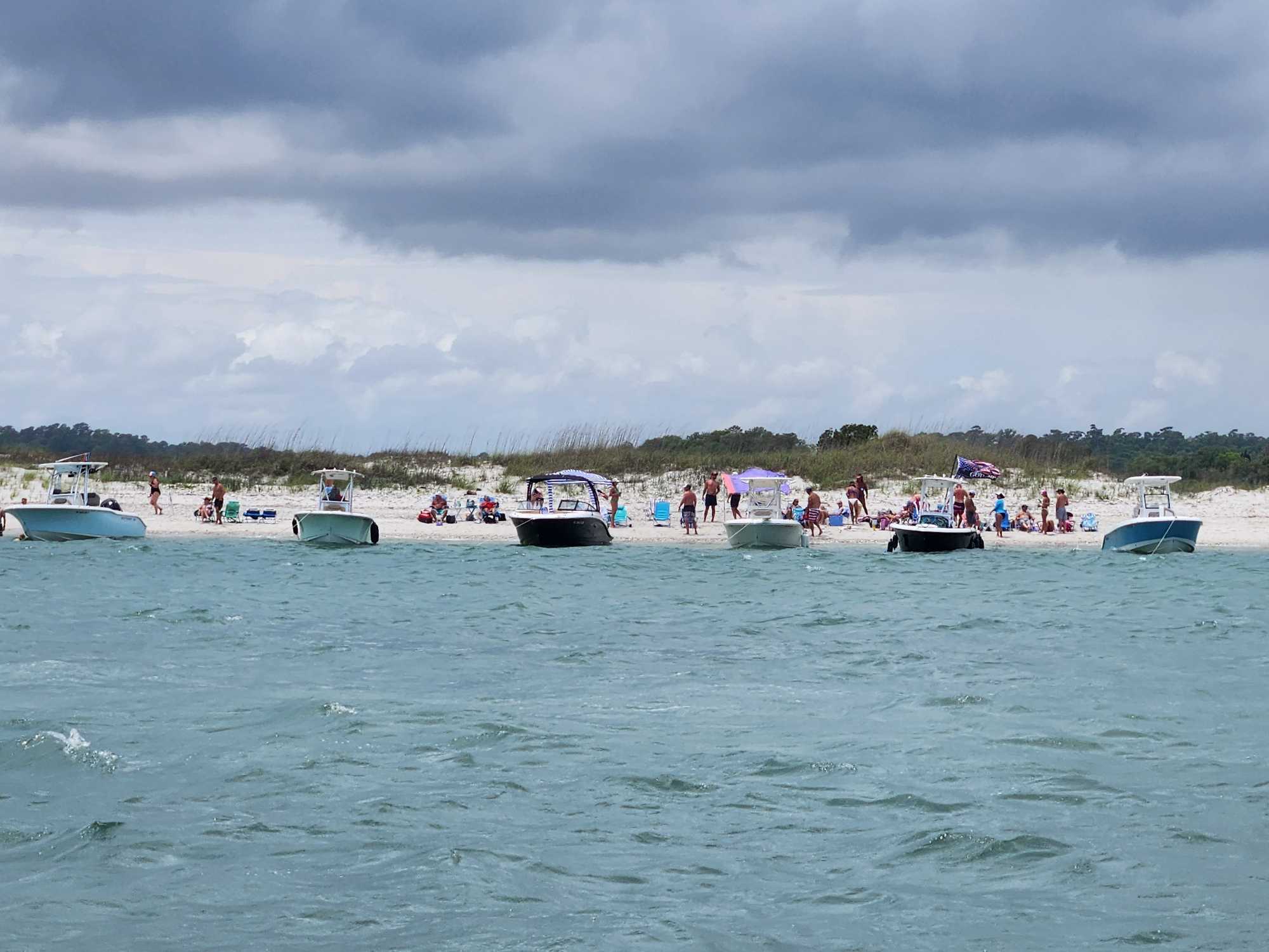 Multiple boats anchored along Carolina Beach NC shoreline with beachgoers enjoying sandy beach under cloudy sky