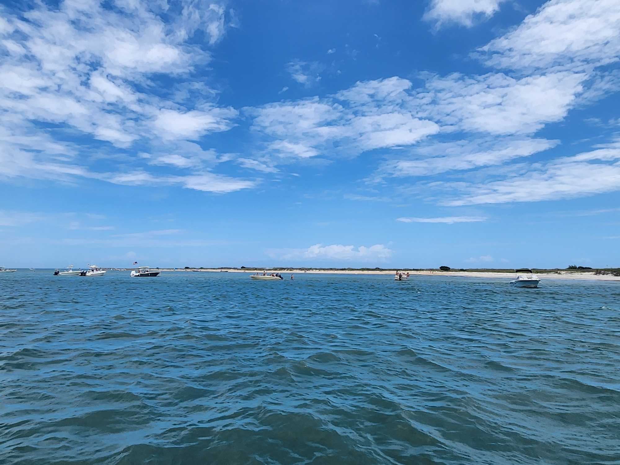 Beautiful blue waters with several boats anchored near Carolina Beach NC coastline under partly cloudy sky