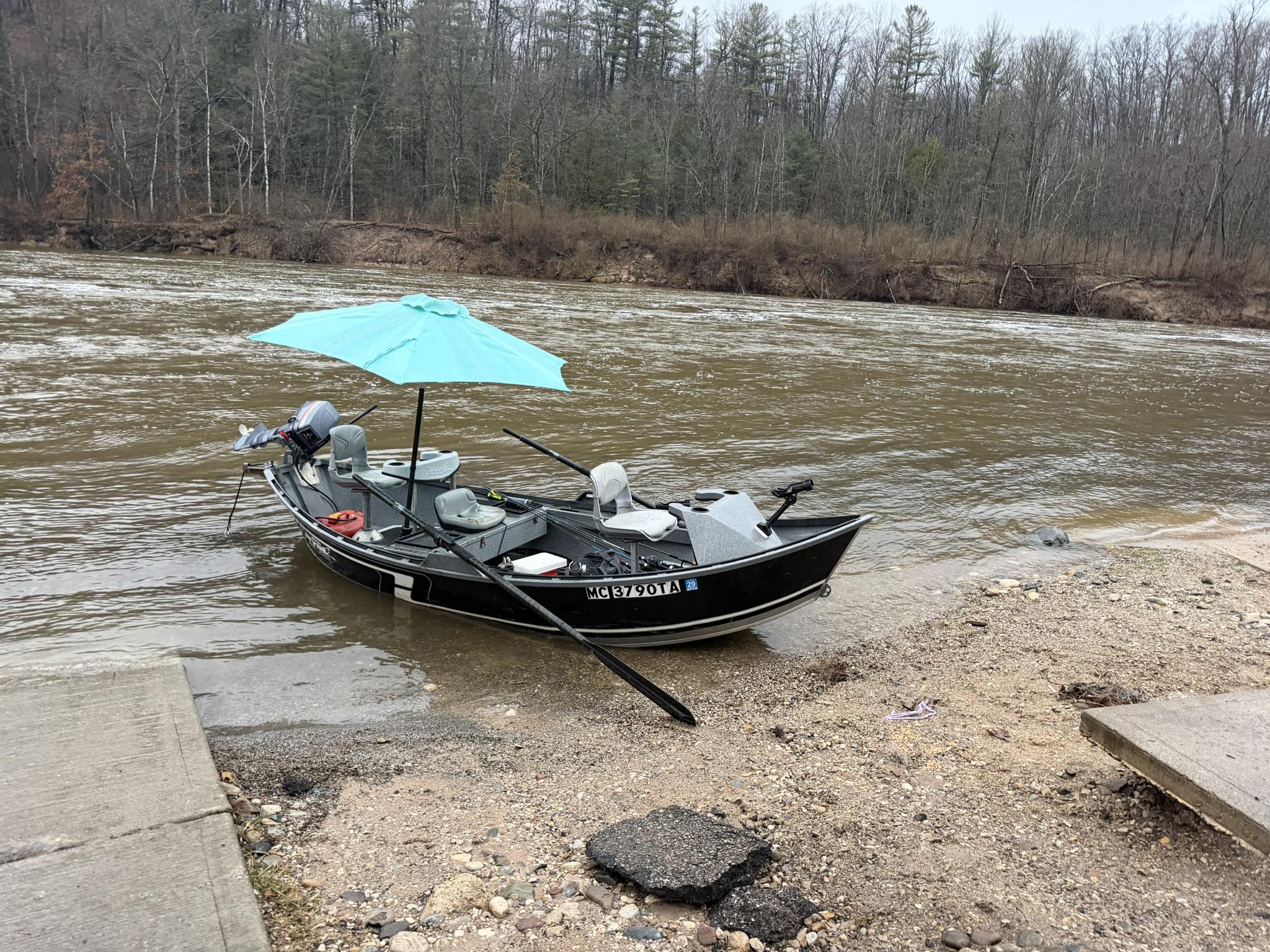 Fishing boat with umbrella docked at muddy riverbank in Brethren MI