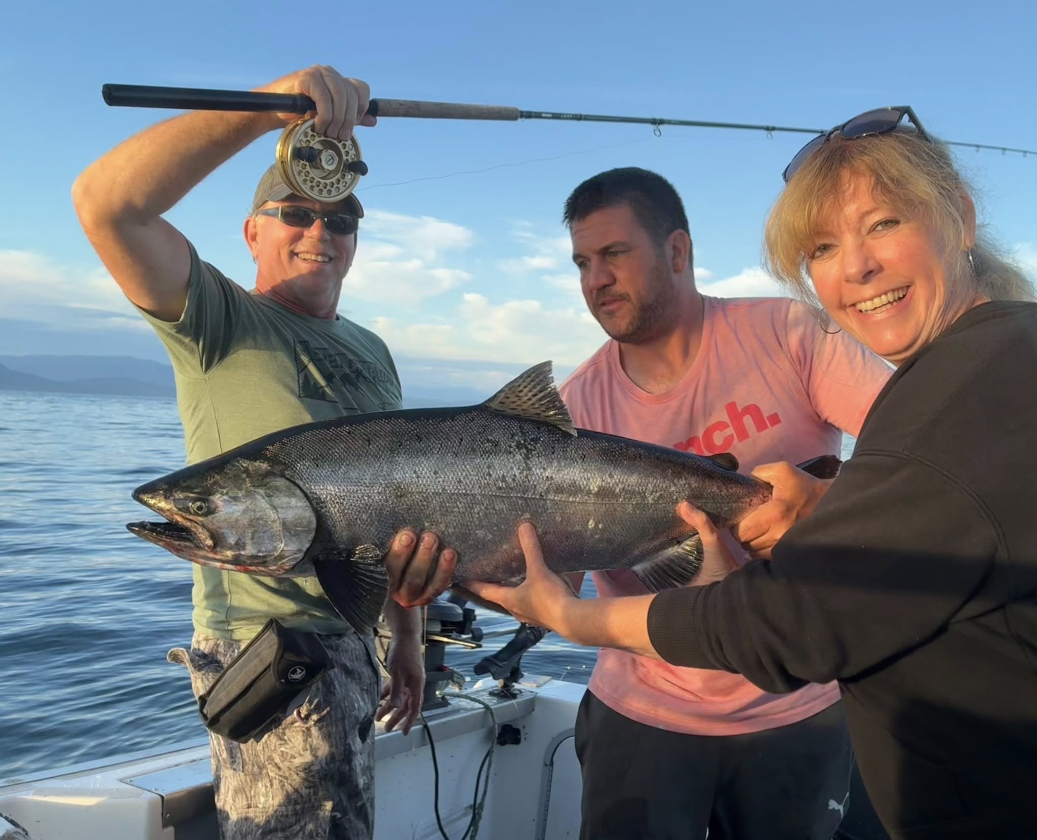Three people holding a large Chinook salmon on a fishing boat in Nanaimo BC waters
