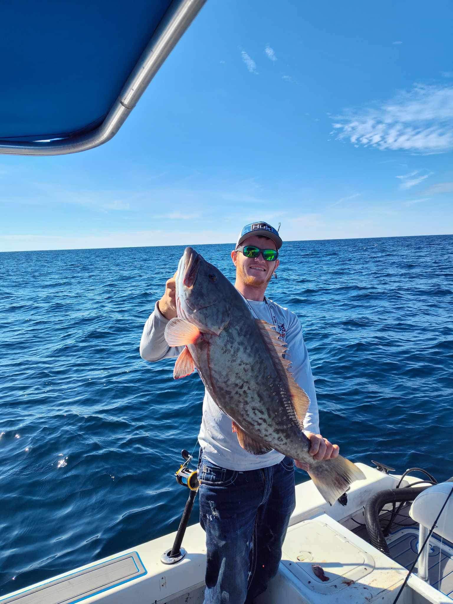 Angler holding large gag grouper on fishing boat in open ocean waters