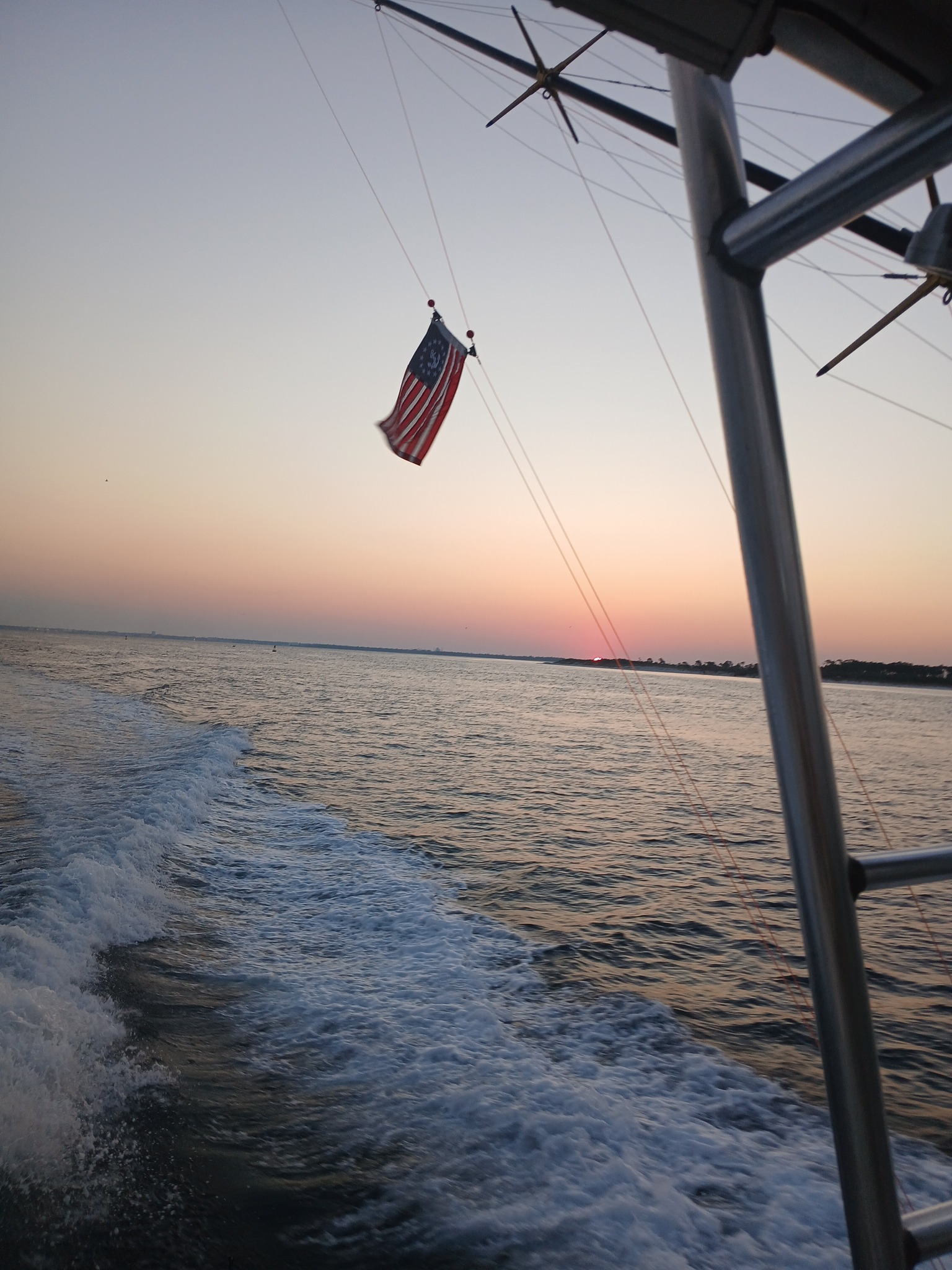 View from fishing boat at sunset showing wake in water and American flag
