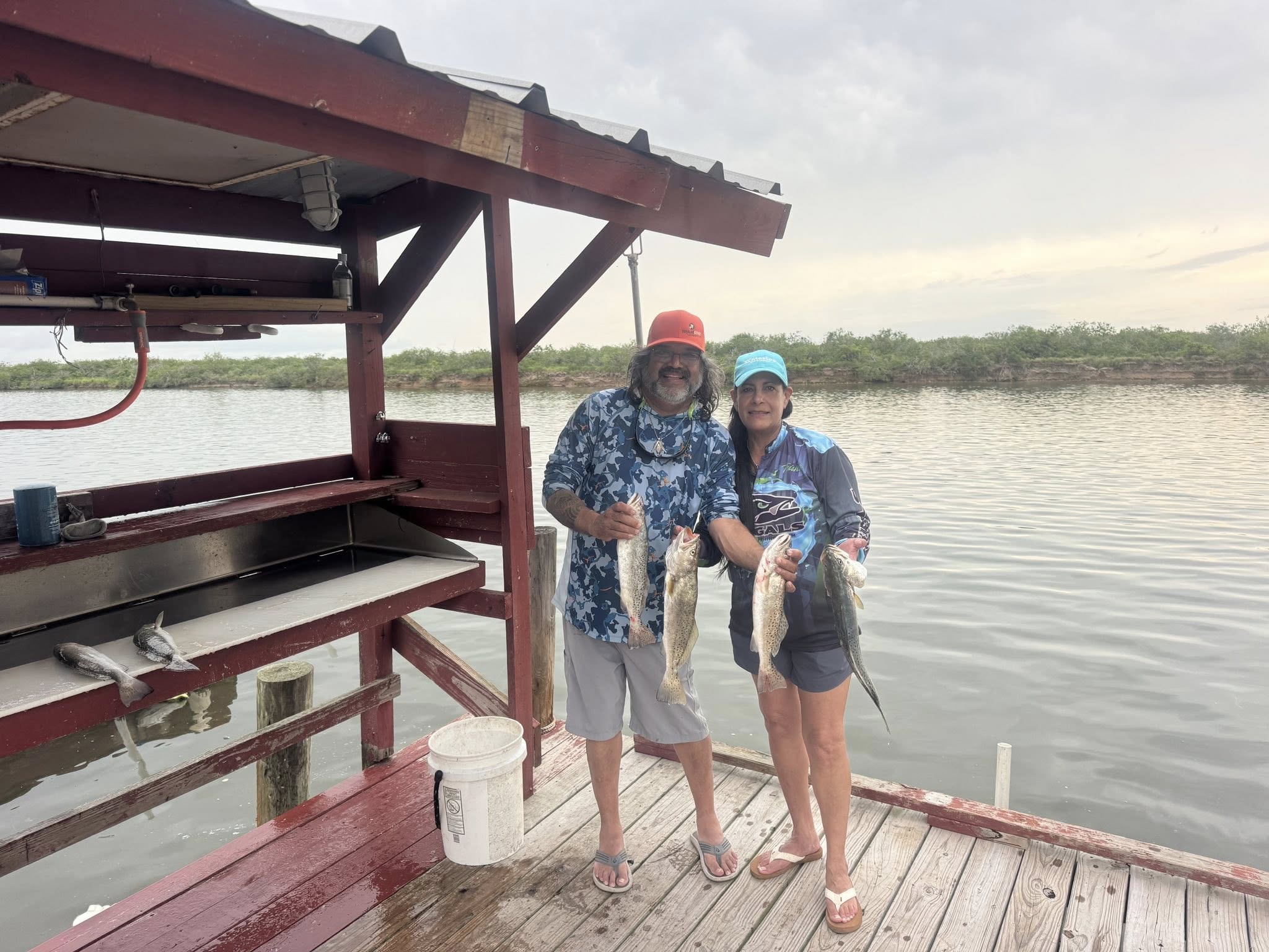 Two anglers displaying caught speckled trout on wooden fishing dock in Arroyo City TX