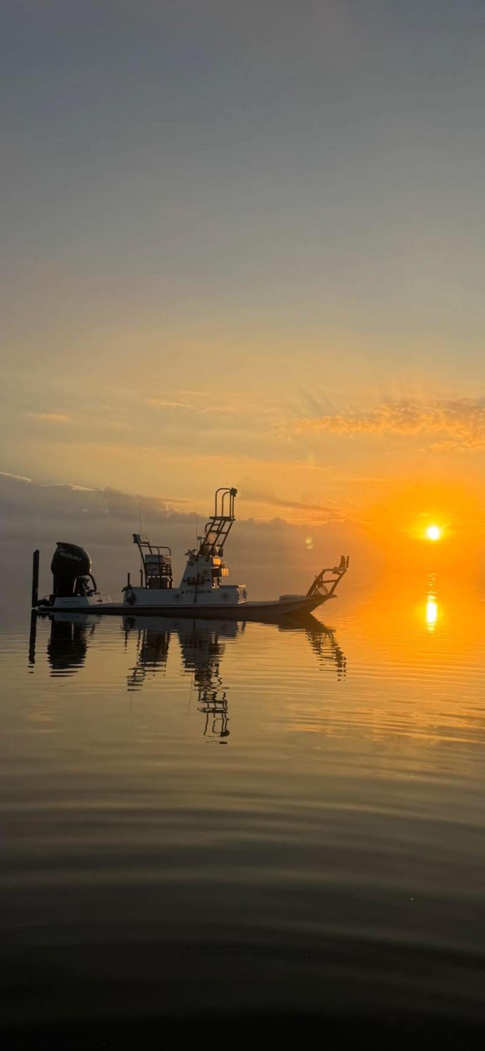 Fishing boat silhouetted against golden sunrise on calm water in Arroyo City TX